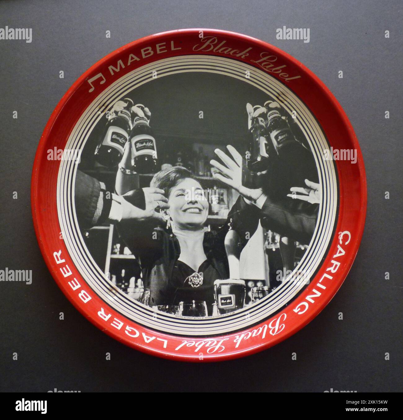 Un plateau à bière vintage des années 1960 fabriqué par le Royaume-Uni par Reginald Corfield Ltd, faisant la promotion de la bière Carling Black Label, en utilisant leur campagne publicitaire «Mabel Black Label». Le plateau est décoré d'une image lithographique d'une barmaid (Mabel) distribuant des bouteilles de lager Carling Black Label à ses clients. Banque D'Images