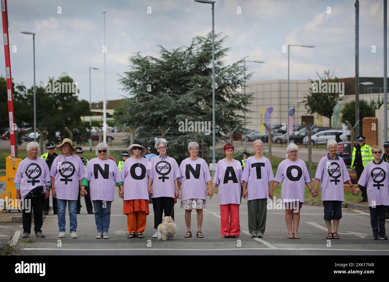 20 juillet 2024, Lakenheath, Angleterre, Royaume-Uni : les manifestants s'alignent de l'autre côté de la route d'accès à la base aérienne pour observer deux minutes de silence pour ceux qui sont morts des suites de la guerre devant la base aérienne de Lakenheath, pendant la manifestation. La manifestation a été organisée par la campagne pour le désarmement nucléaire (CND), dont les partisans s'opposent au retour potentiel des armes nucléaires dans les bases militaires au Royaume-Uni, telles que la RAF Lakenheath après qu'il a été signalé que les États-Unis ont l'intention de résister aux bombes nucléaires sur la base. Après une protestation soutenue, les armes nucléaires ont été retirées de Lakenheath en 2008. (Image crédit : Banque D'Images