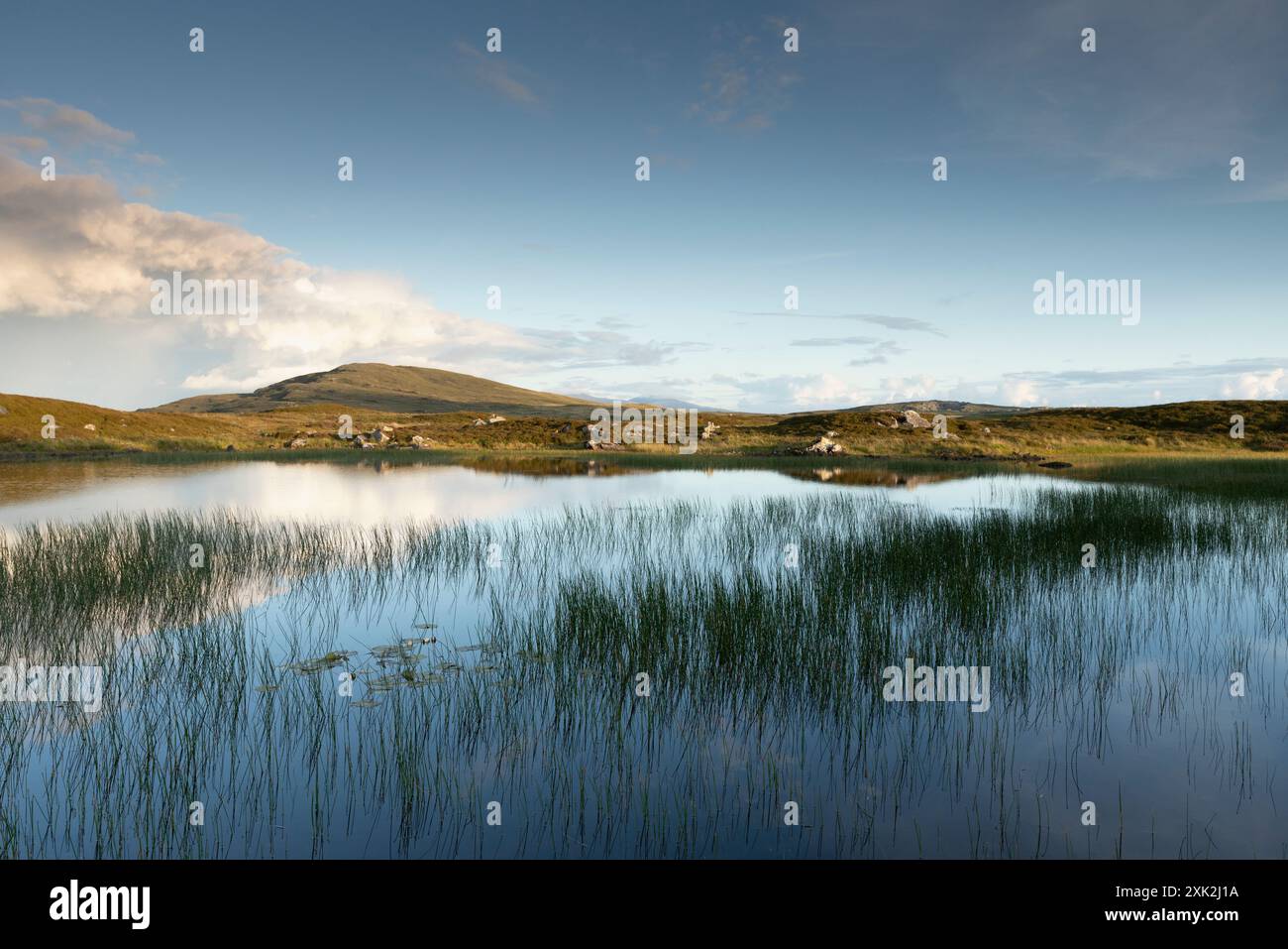 Colline Rueval sur l'île de Benbecula, reflétée dans un loch d'eau douce calme dans les ares Gramsdale de l'île. Collines de South Uist en arrière-plan. Banque D'Images