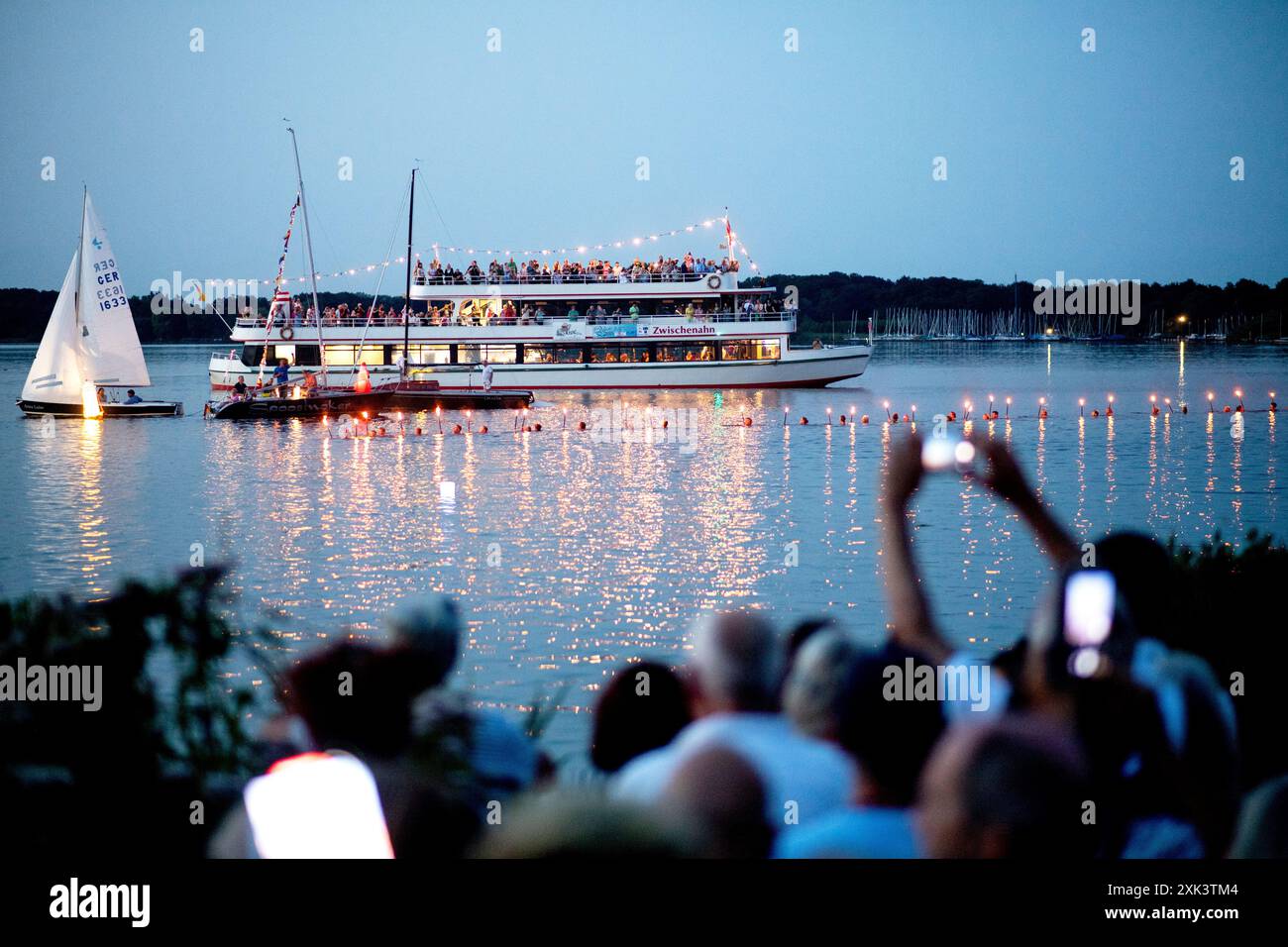 Bad Zwischenahn, Allemagne. 20 juillet 2024. De nombreux visiteurs regardent environ 100 nageurs du DLRG nager dans l'eau avec des torches allumées pendant la nuit des lumières. Dans le cadre de la nuit des lumières, les jardins du spa de Bad Zwischenahn se transforment en une mer de couleurs. Crédit : Hauke-Christian Dittrich/dpa/Alamy Live News Banque D'Images