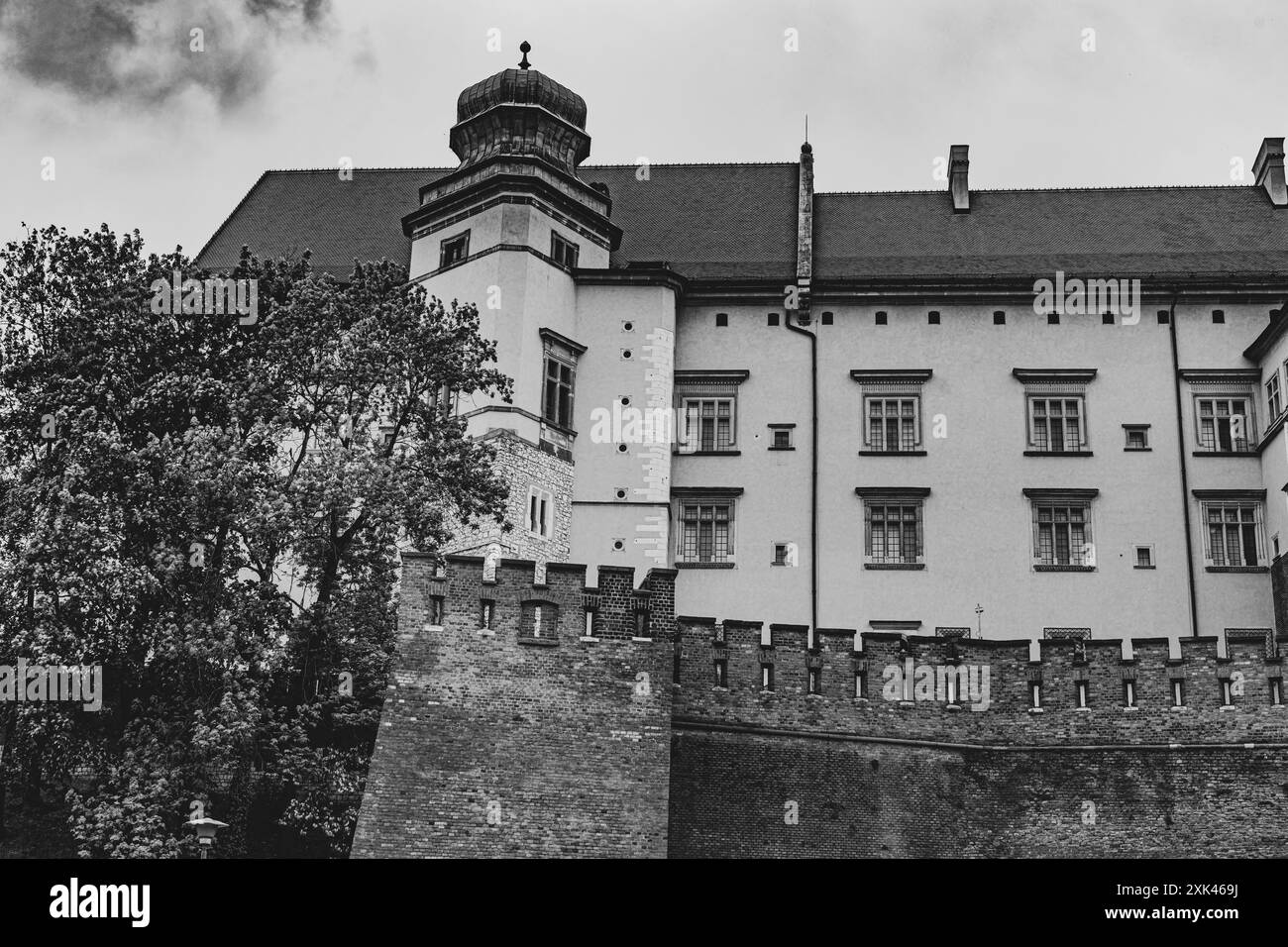 Une photo en noir et blanc d'un château historique avec des arbres et un ciel nuageux à Cracovie Banque D'Images