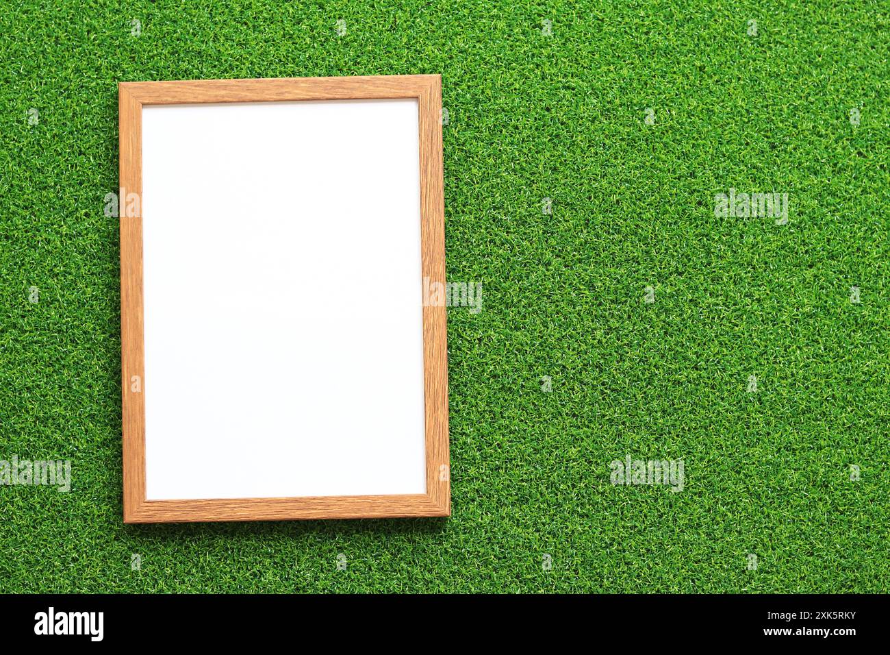 Cadre vide pour photo ou texte avec une feuille blanche sur un fond d'herbe verte. Feuille d'herbe verte artificielle et cadre en bois simple. Placer pour le texte Banque D'Images