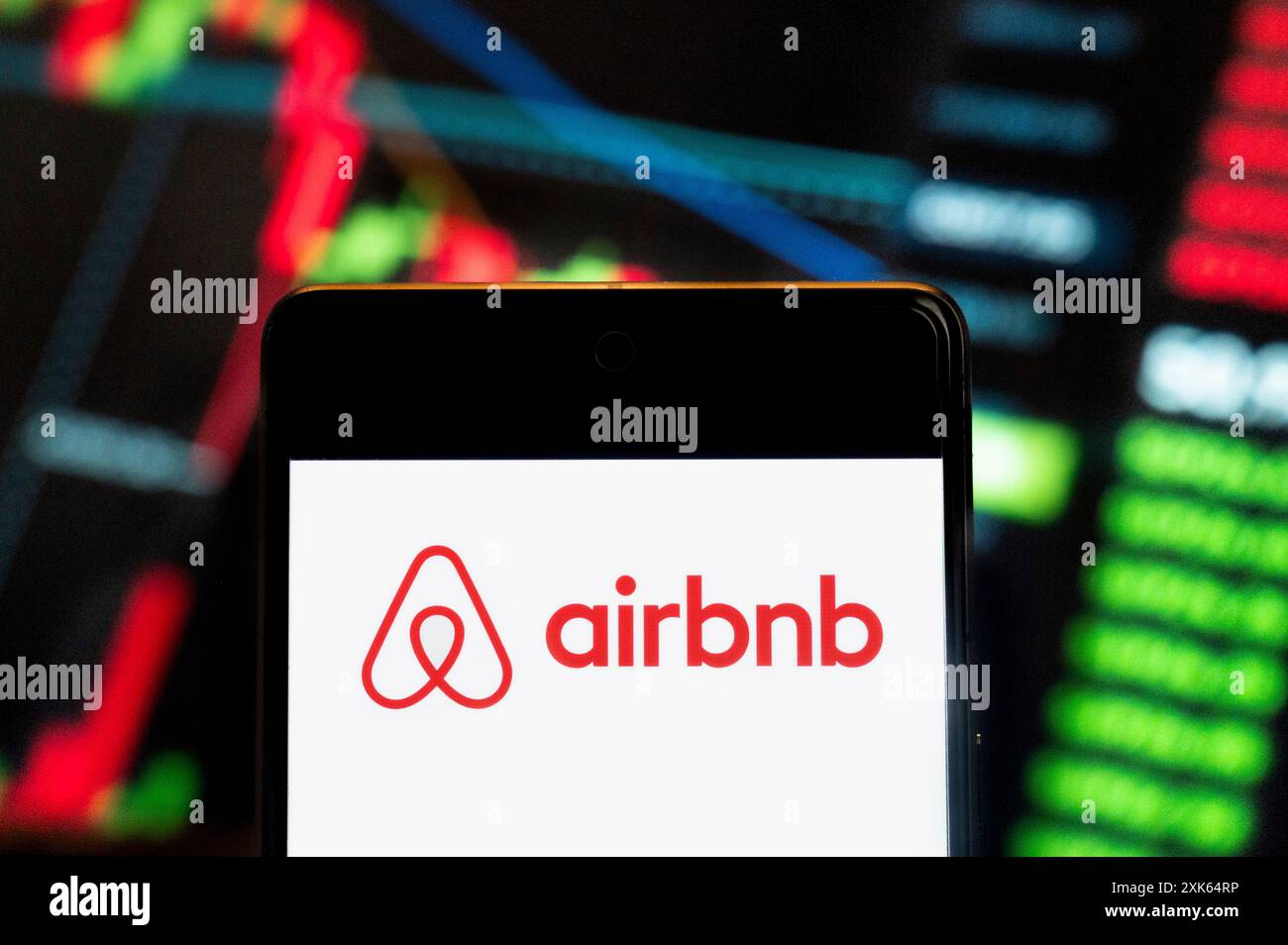 Dans cette illustration photo, le logo de la place de marché en ligne américaine et du service hôtelier Airbnb (NASDAQ : ABNB) vu sur un smartphone avec un graphique de l'indice boursier économique en arrière-plan. Banque D'Images