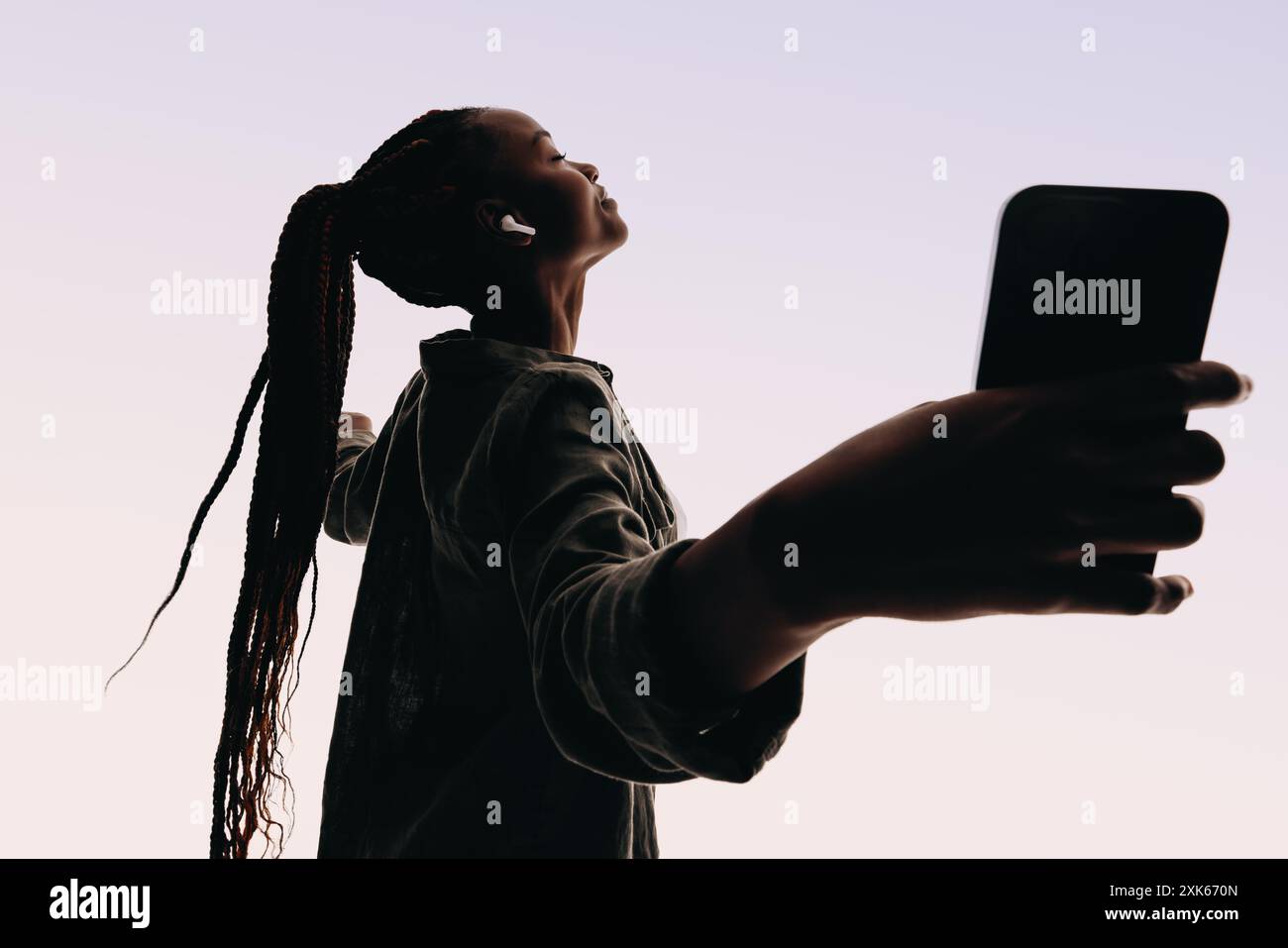 Femme avec des tresses, expression heureuse, et écouteurs connectés à son téléphone portable. Elle danse et bouge de manière ludique, profitant du flux de la musique pendant que stan Banque D'Images