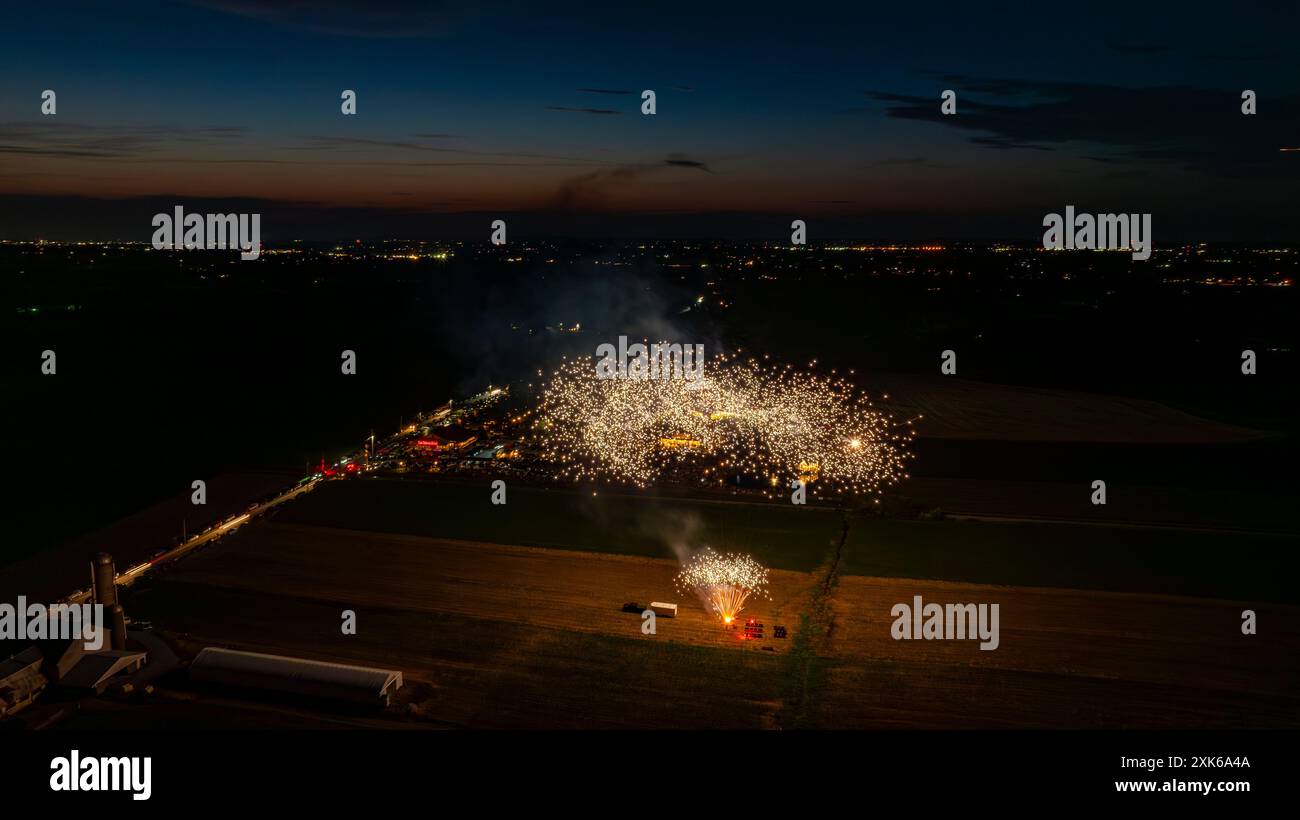 Feux d'artifice dorés création d'Un nuage étincelant dense dans le ciel nocturne, illuminant Un rassemblement avec des tentes et les lumières lointaines de la ville, avec Un horizon crépusculaire ajoutant à la scène festive. Banque D'Images