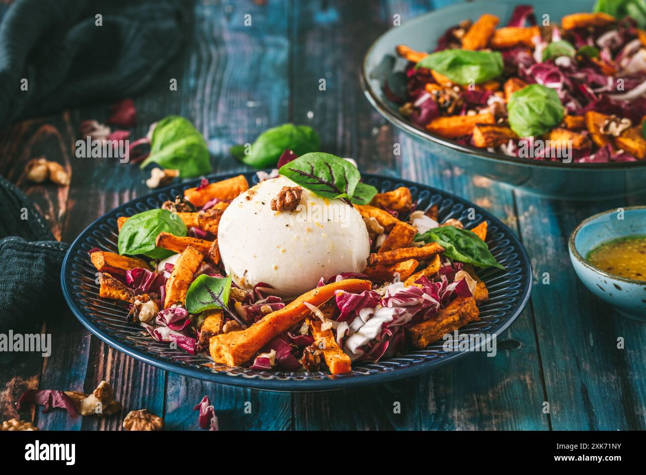 Salade de radicchio avec des bâtonnets de patates douces rôties, des noix et du fromage burrata sur fond de bois bleu rustique Banque D'Images