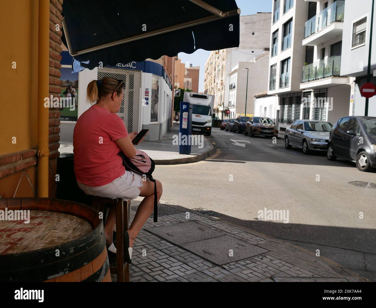 Femme assise à l'extérieur d'un bar au coin de la rue, vérifiant son téléphone. Malaga, Espagne Banque D'Images
