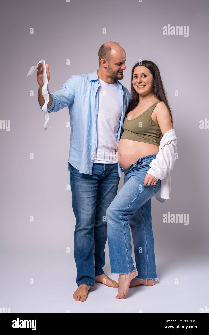 Une femme enceinte dans une chemise blanche, un Jean bleu avec le ventre exposé et son mari tiennent une photo de leur nouveau-né à naître. Grossesse, mites Banque D'Images