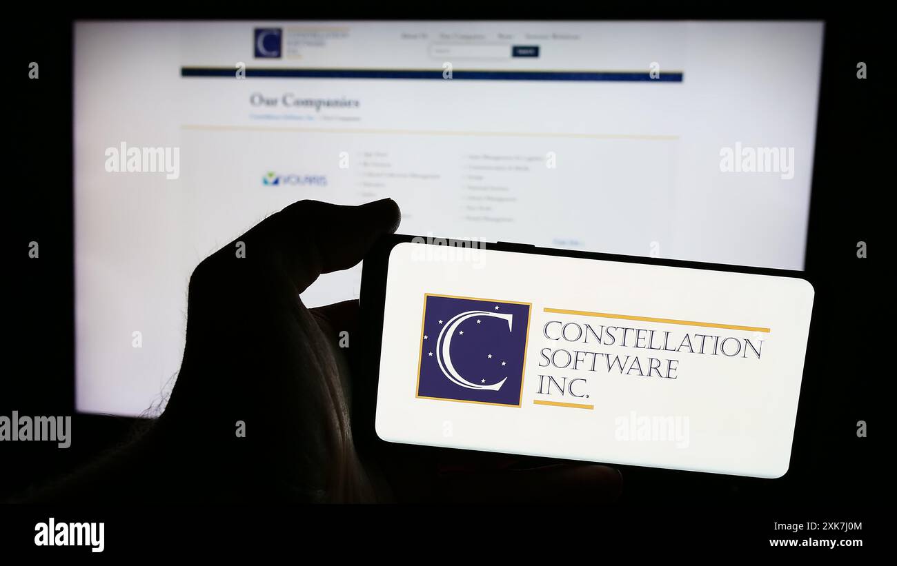 Personne tenant un téléphone intelligent avec le logo de la société canadienne Constellation Software Inc devant le site Web. Concentrez-vous sur l'affichage du téléphone. Banque D'Images
