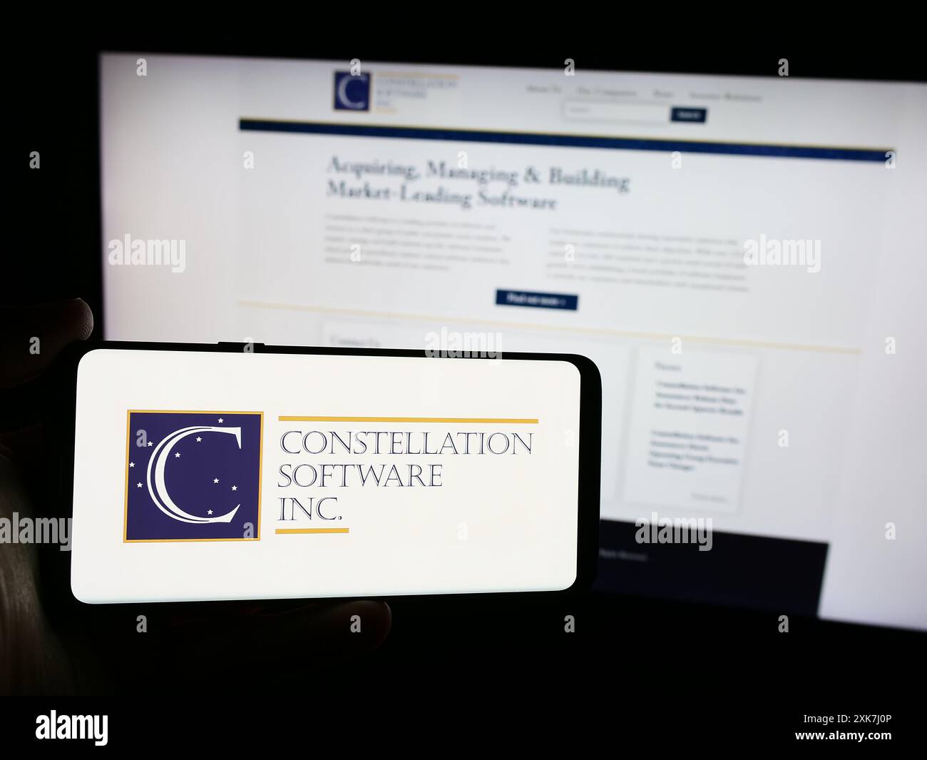 Personne tenant un téléphone cellulaire avec le logo de la société canadienne Constellation Software Inc devant la page Web de l'entreprise. Concentrez-vous sur l'affichage du téléphone. Banque D'Images