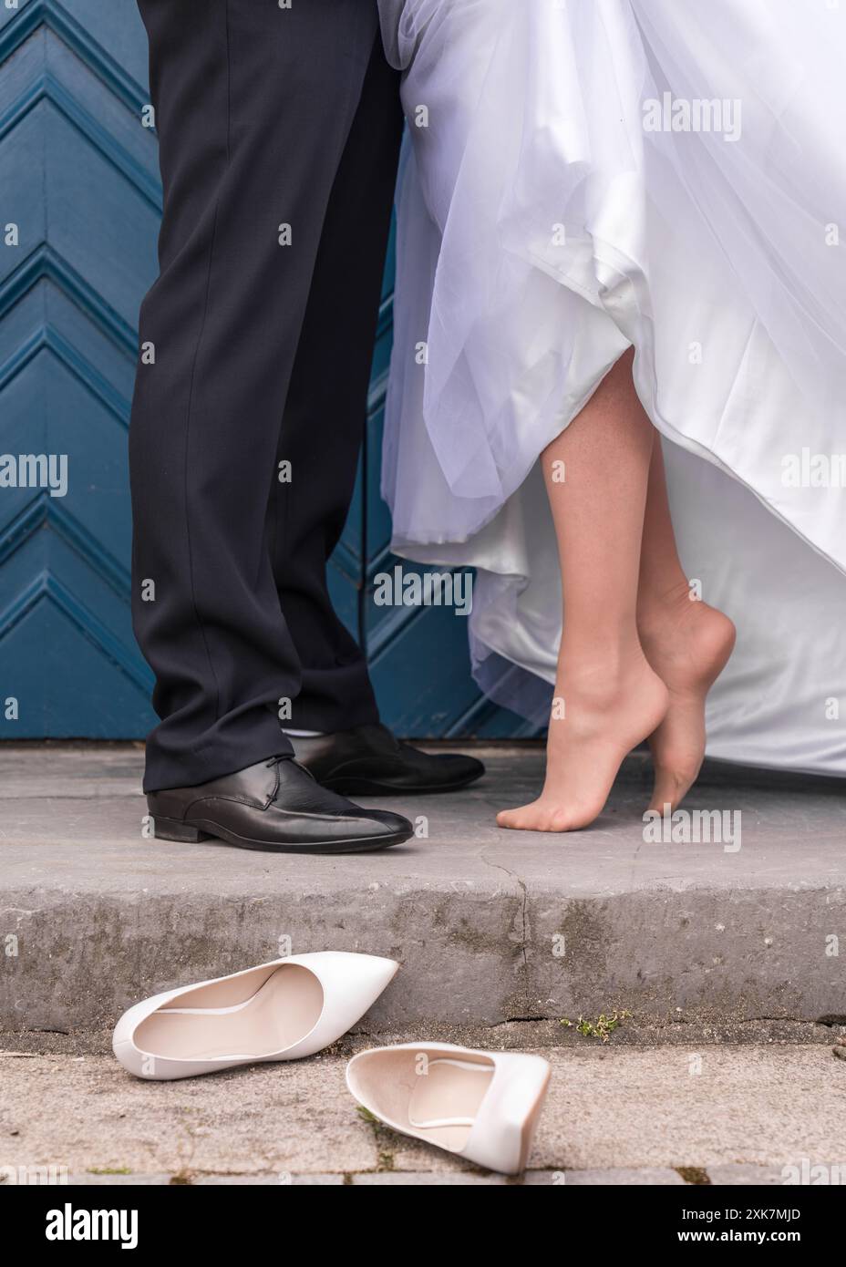 Détails du mariage. Un couple de mariage sur un fond de portes bleues. Seuls les pieds du jeune couple, la mariée se tient sans chaussures, chaussures de mariage Banque D'Images