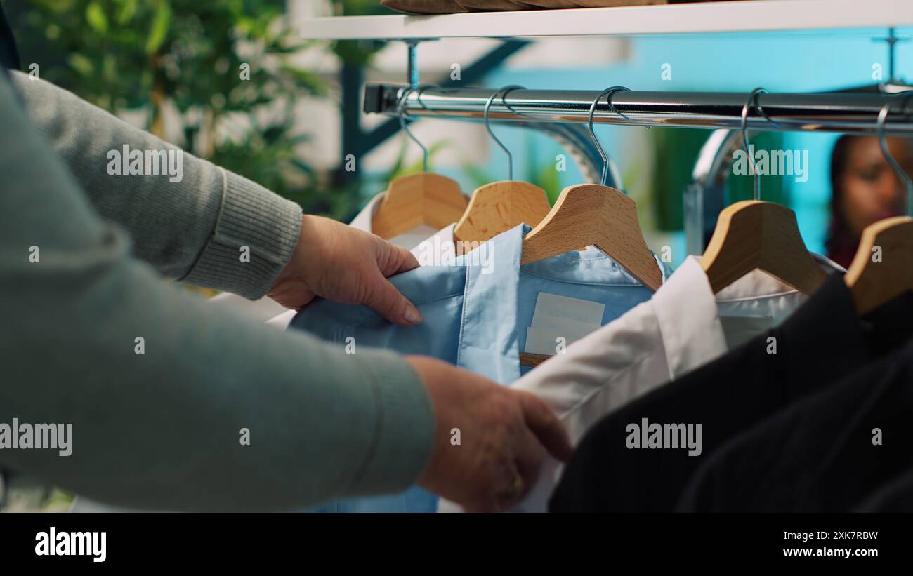 Femme senior cherchant des vêtements pour son mari, à la recherche de costumes élégants sur cintres au grand magasin. Couple de personnes âgées magasinant pour la nouvelle collection de mode au showroom. Caméra A. Banque D'Images