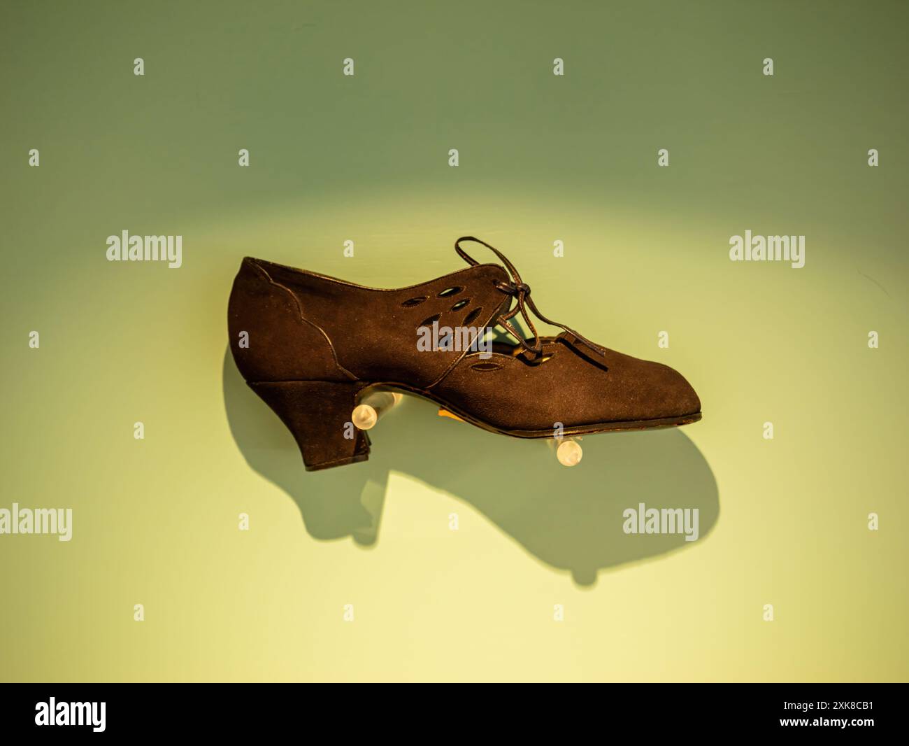 Une chaussure vintage féminine à talons bas en brun foncé avec des détails découpés complexes et un design à lacets est exposée sur un support clair sur un fond vert, mettant en valeur son savoir-faire et son élégance Banque D'Images