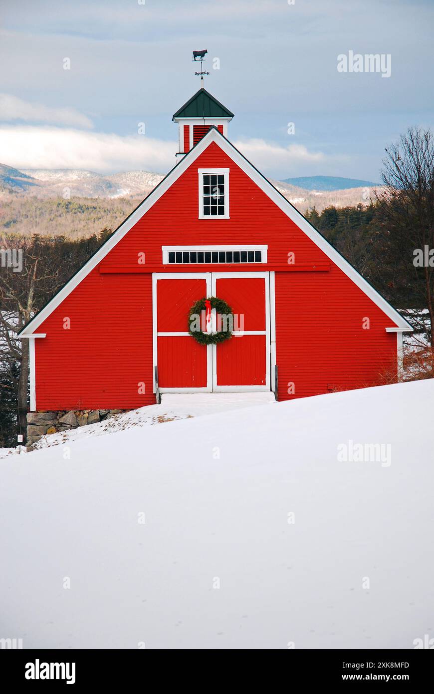 Une grange rouge entourée de neige hivernale est décorée d'une couronne de Noël dans les hautes terres de la Nouvelle-Angleterre Banque D'Images