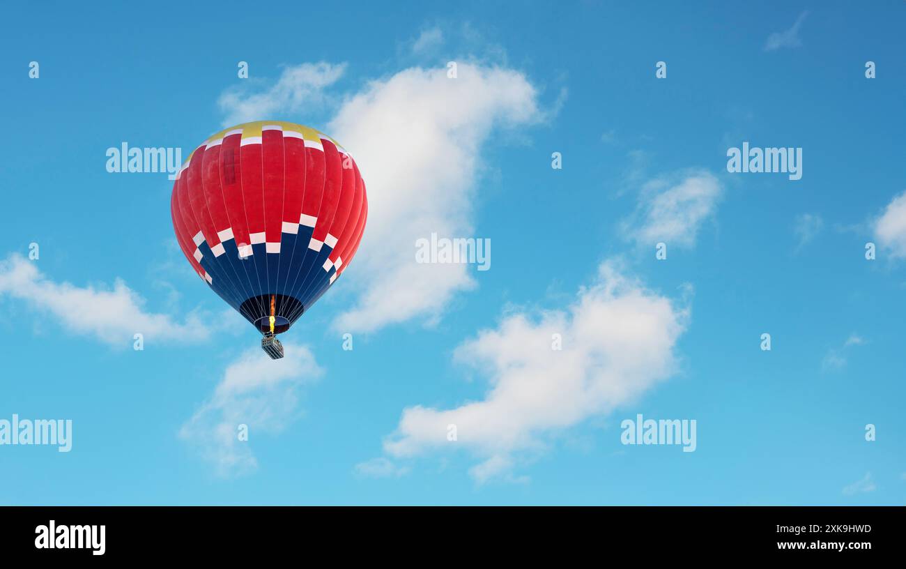 Montgolfière en bleu foncé, rouge et jaune volant dans un ciel bleu légèrement nuageux Banque D'Images