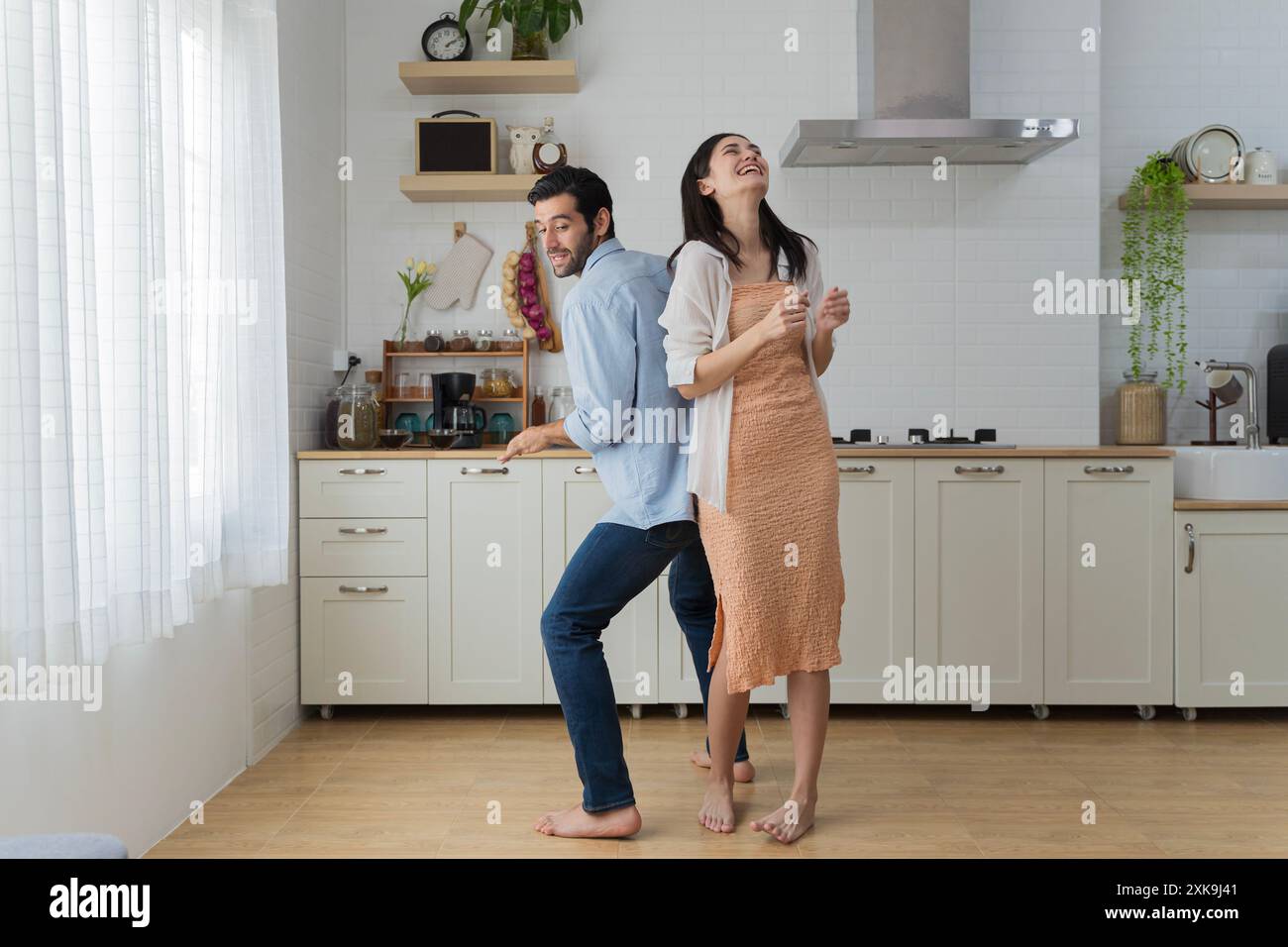 Heureux mari et femme milléniaux dansant dans la cuisine moderne célébrer l'anniversaire de mariage à la maison ensemble, heureux jeunes locataires de couple ont du plaisir en Banque D'Images