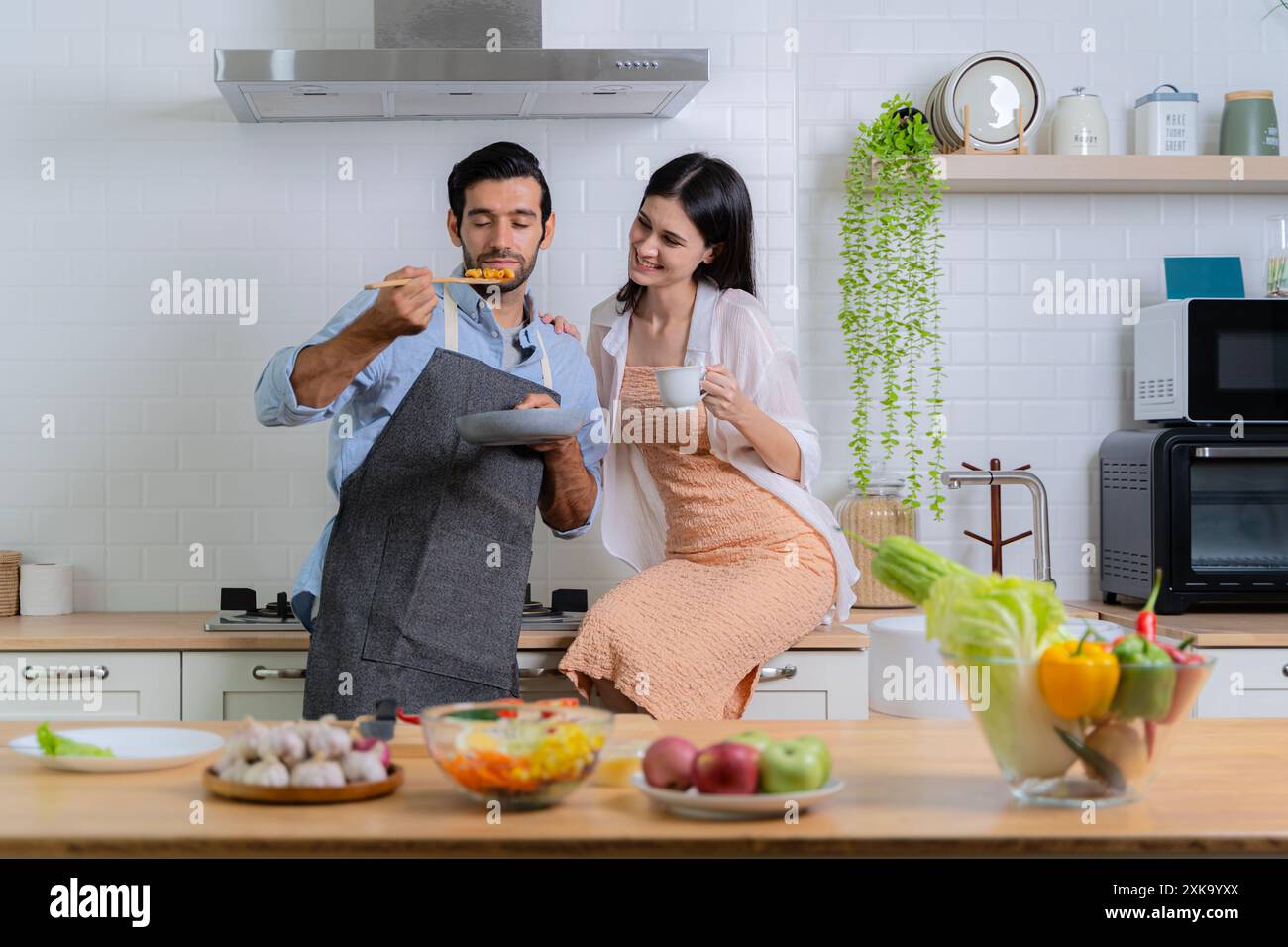 L'homme qui inhalait l'odeur du petit déjeuner en cours de préparation avec sa petite amie à proximité. Couple amoureux s'amuser tout en préparant un petit déjeuner ensemble Banque D'Images