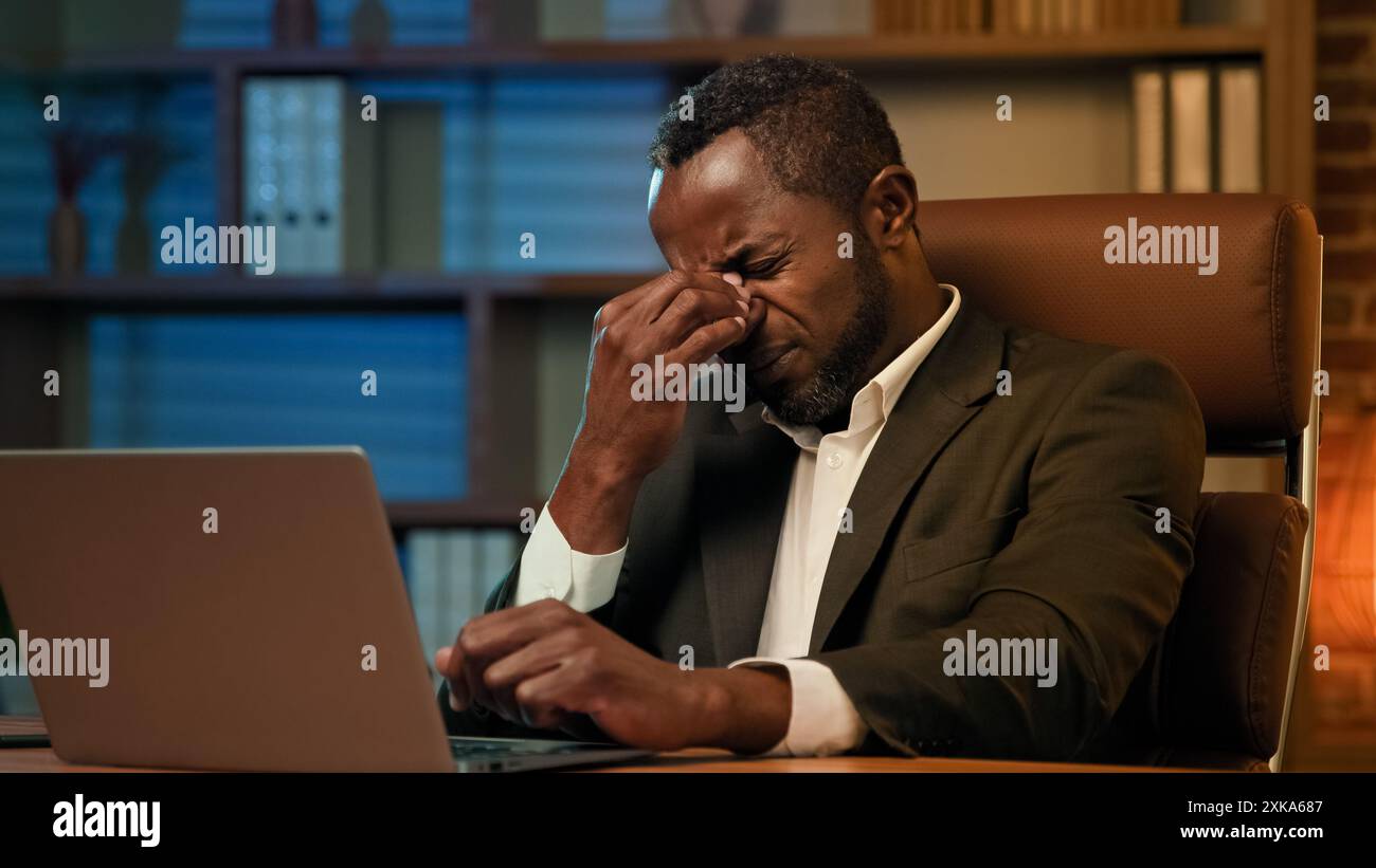 Homme d'affaires afro-américain adulte travaillant sur ordinateur portable dans le bureau homme fatigué malsain souffrant de maux de tête ressent la fatigue de pression de douleur du surmenage Banque D'Images
