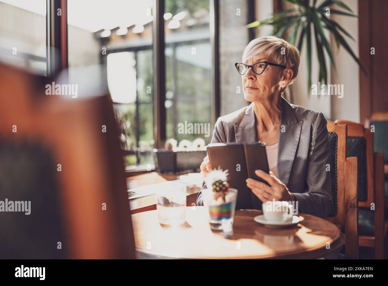 Femme mature est assise dans le café et relaxant. Elle boit du café et utilise une tablette numérique. Banque D'Images