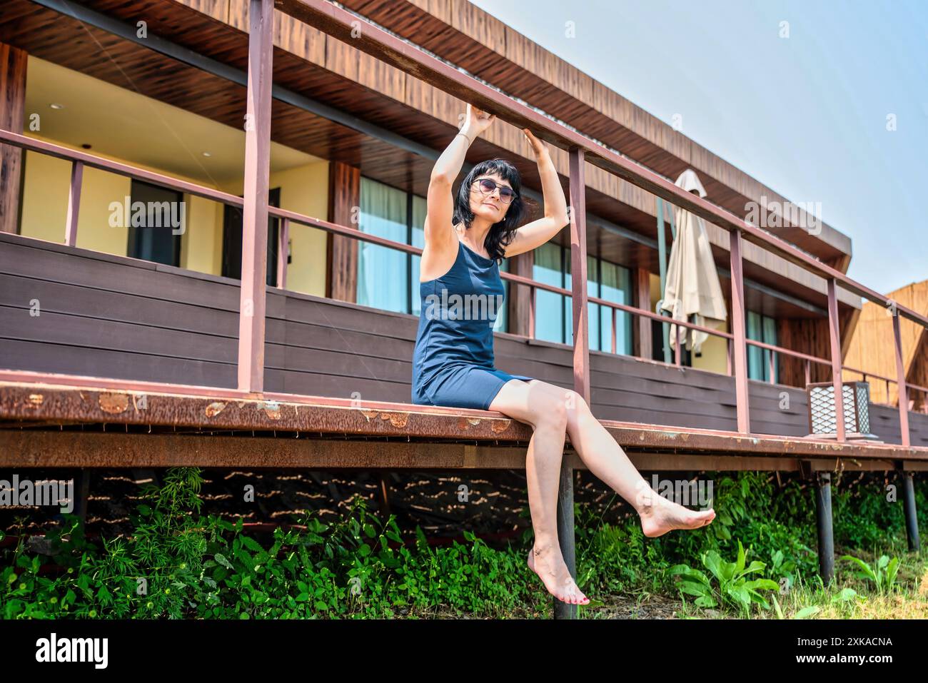 femme russe de 50 ans en robe courte et lunettes de soleil assis sur un balcon et profitant le jour d'été Banque D'Images