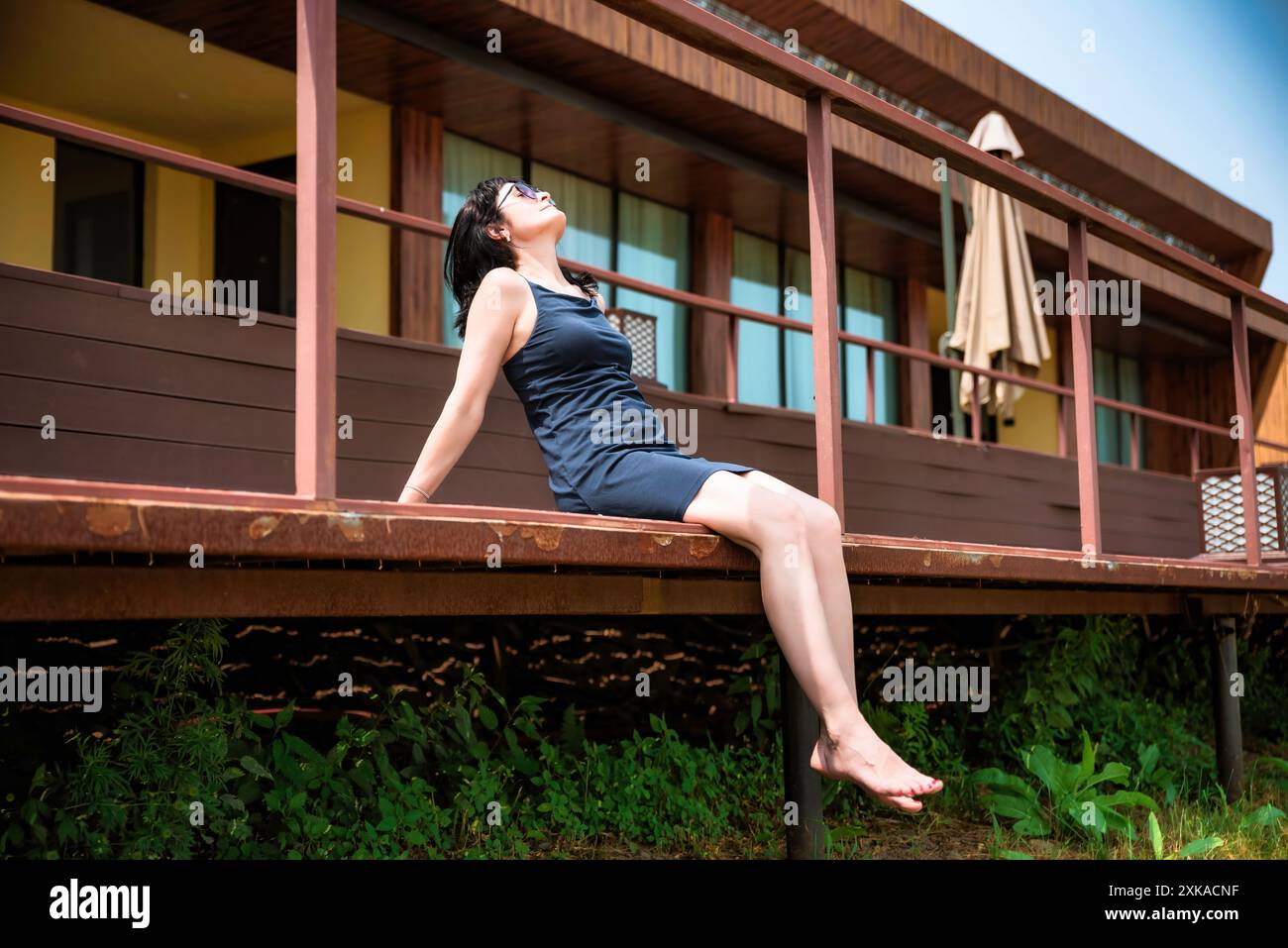 femme russe de 50 ans en robe courte et lunettes de soleil assis sur un balcon et profitant le jour d'été Banque D'Images