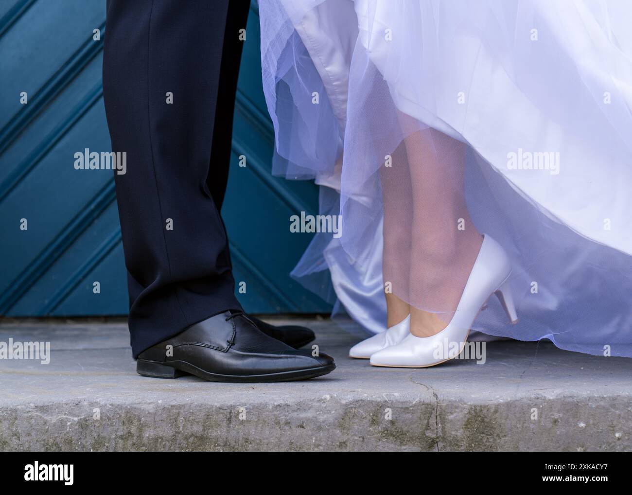 Détails du mariage. Couple de mariage sur fond de portes bleues. La mariée se tient sur la pointe des pieds. Seulement les jambes d'un jeune couple Banque D'Images