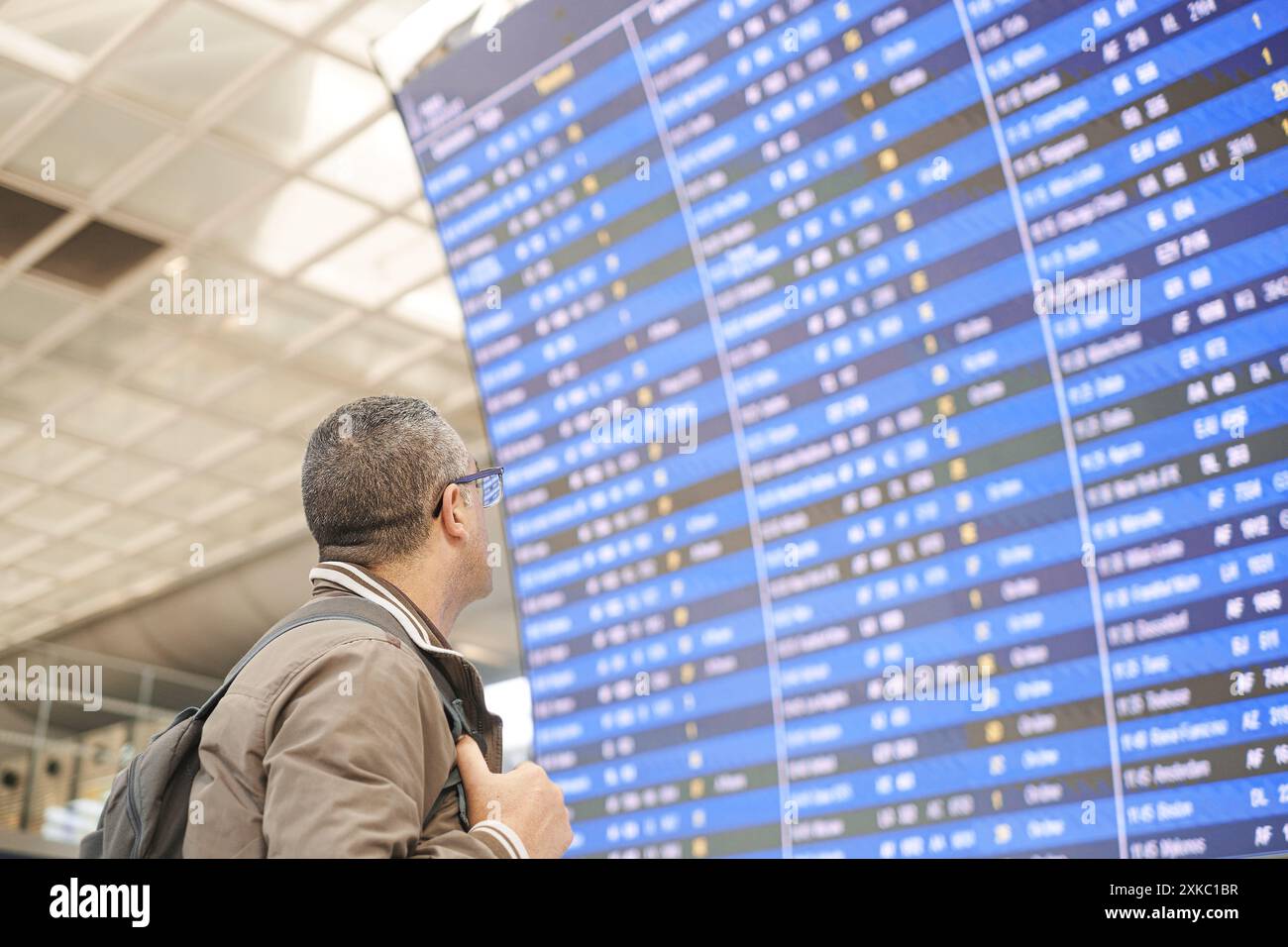 Voyageur avec un sac à dos regarde le panneau d'information des départs et arrivées à l'aéroport Banque D'Images
