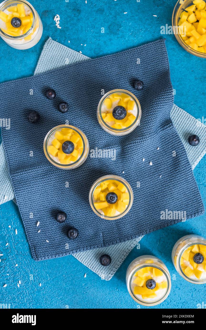 Pudding de riz à la mangue dans des verres à dessert sur fond bleu, dessert d'été, vue de dessus Banque D'Images