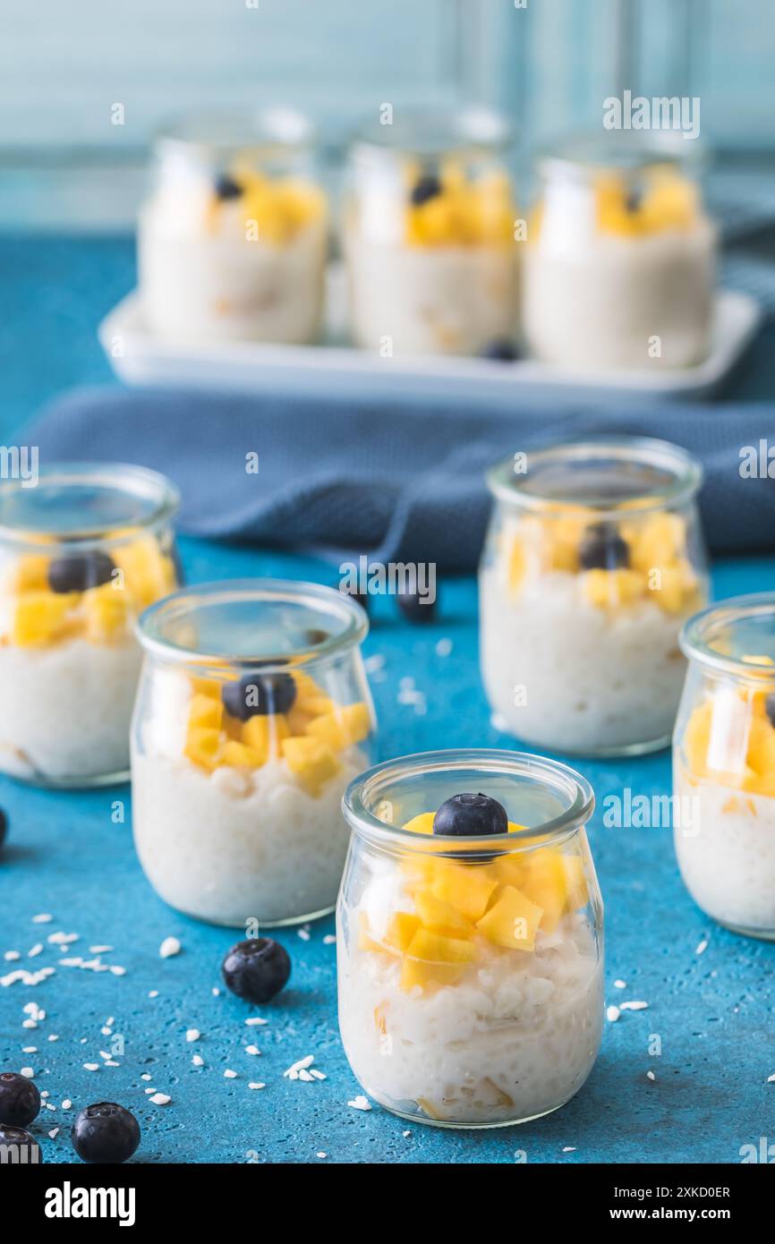 Pudding de riz à la mangue dans des verres à dessert sur fond bleu, dessert d'été, vertical Banque D'Images