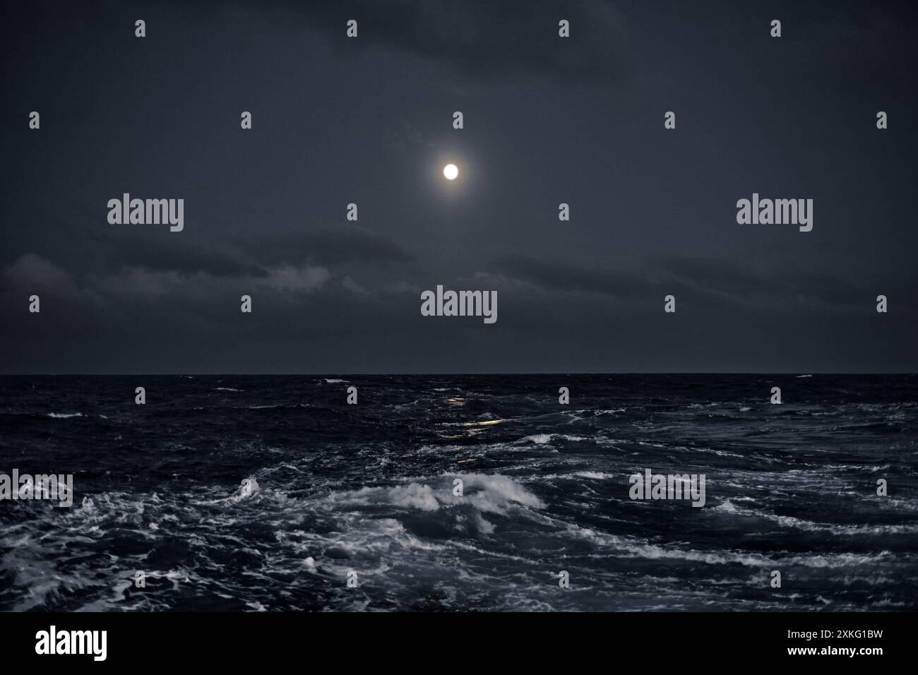 Pleine lune dans le ciel au-dessus de la mer avec des vagues la nuit. Banque D'Images