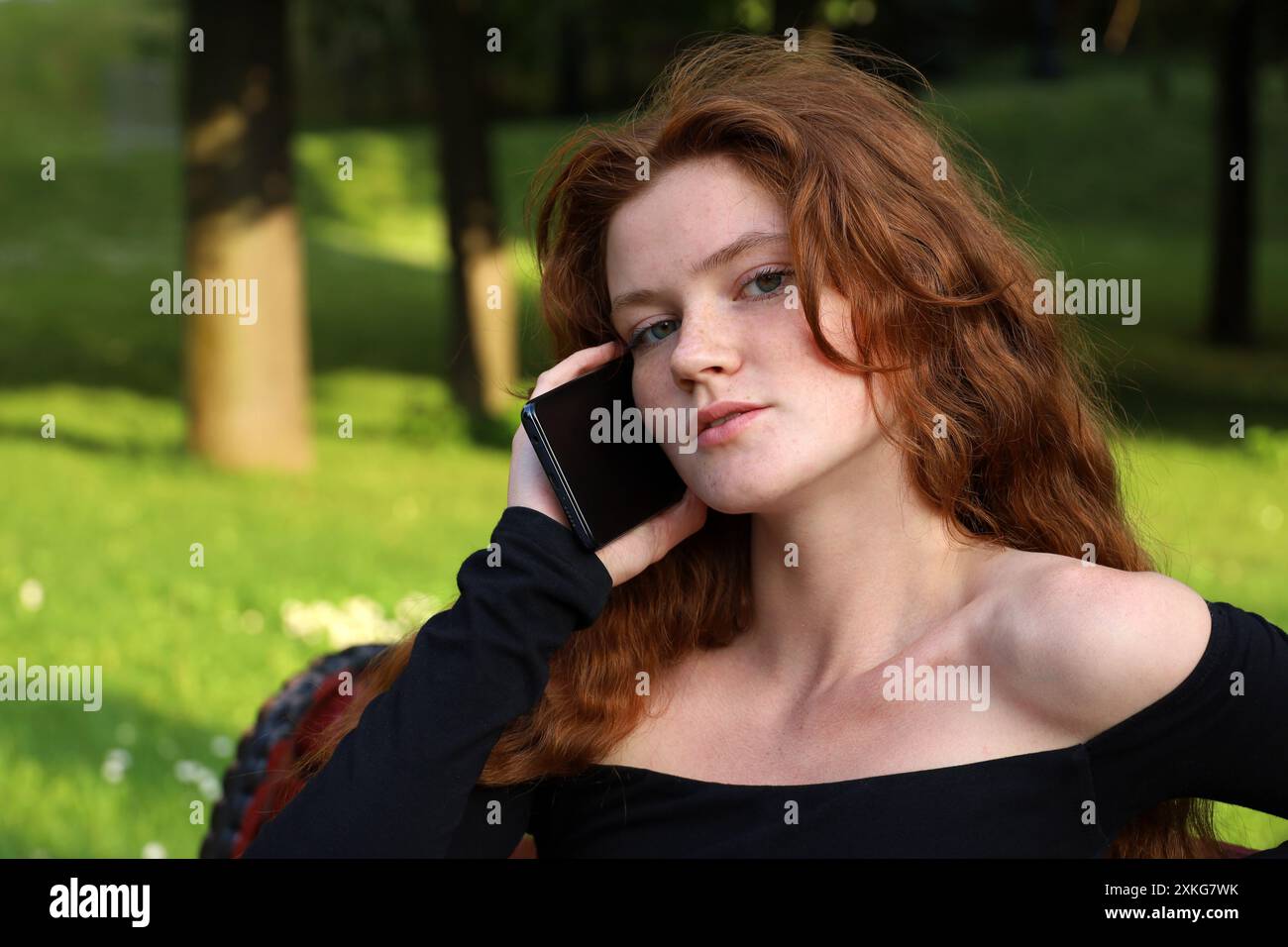 Fille attrayante avec de longs cheveux de gingembre parlant sur le téléphone portable dans le parc d'été Banque D'Images