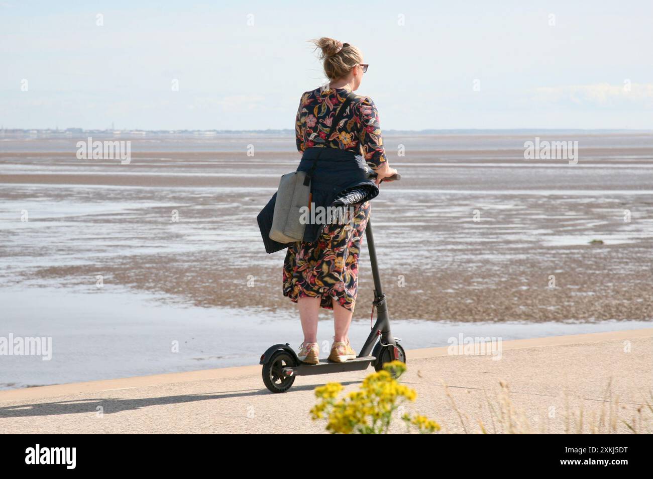 Une dame sur un E-scooter, course le long du front de mer Banque D'Images