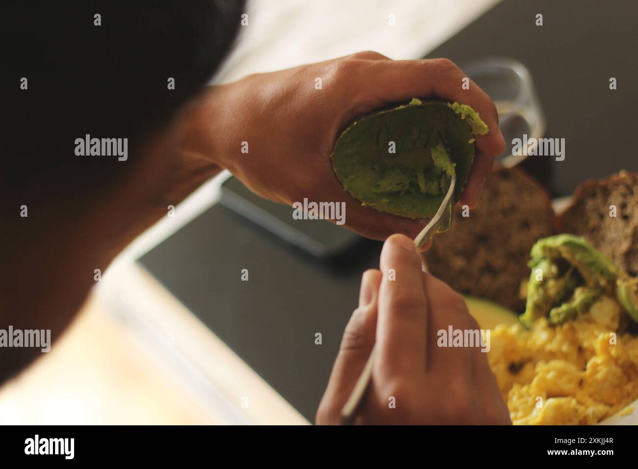 Une image détaillée capturant les mains dans l'acte de manger de l'avocat et des œufs. Parfait pour les thèmes liés à l'alimentation, la nutrition et l'alimentation saine Banque D'Images