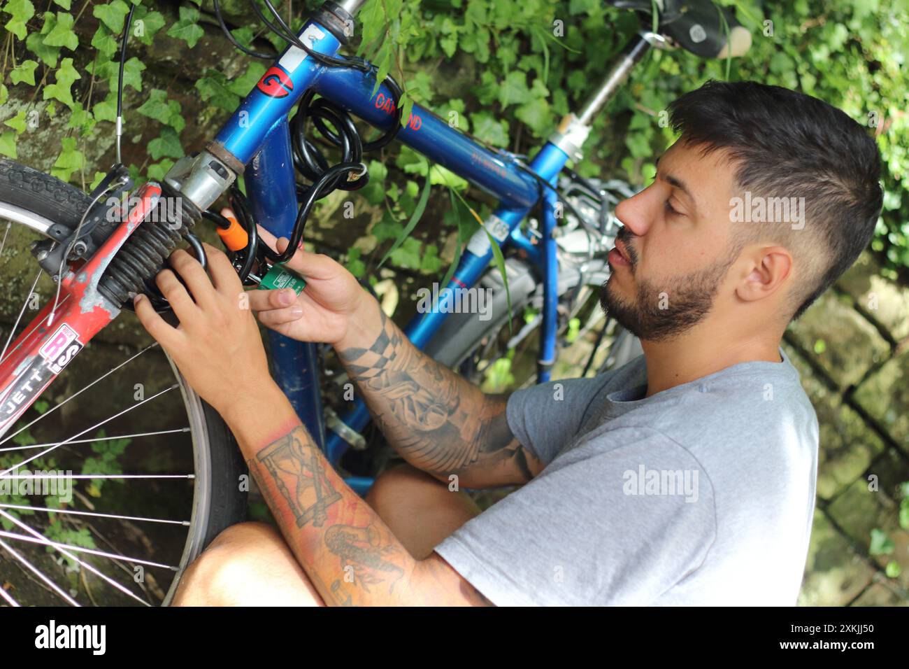 Une image dynamique capturant un jeune homme tatoué alors qu'il déverrouille son vieux vélo. Parfait pour les thèmes liés à la vie urbaine, le cyclisme et le style personnel Banque D'Images