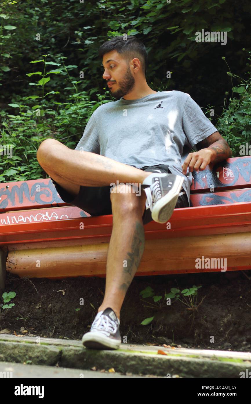 Une image vivante montrant un jeune homme tatoué en vêtements de sport, l'air ennuyé et attendant sur un banc par une journée ensoleillée dans la ville de Zurich. Banque D'Images