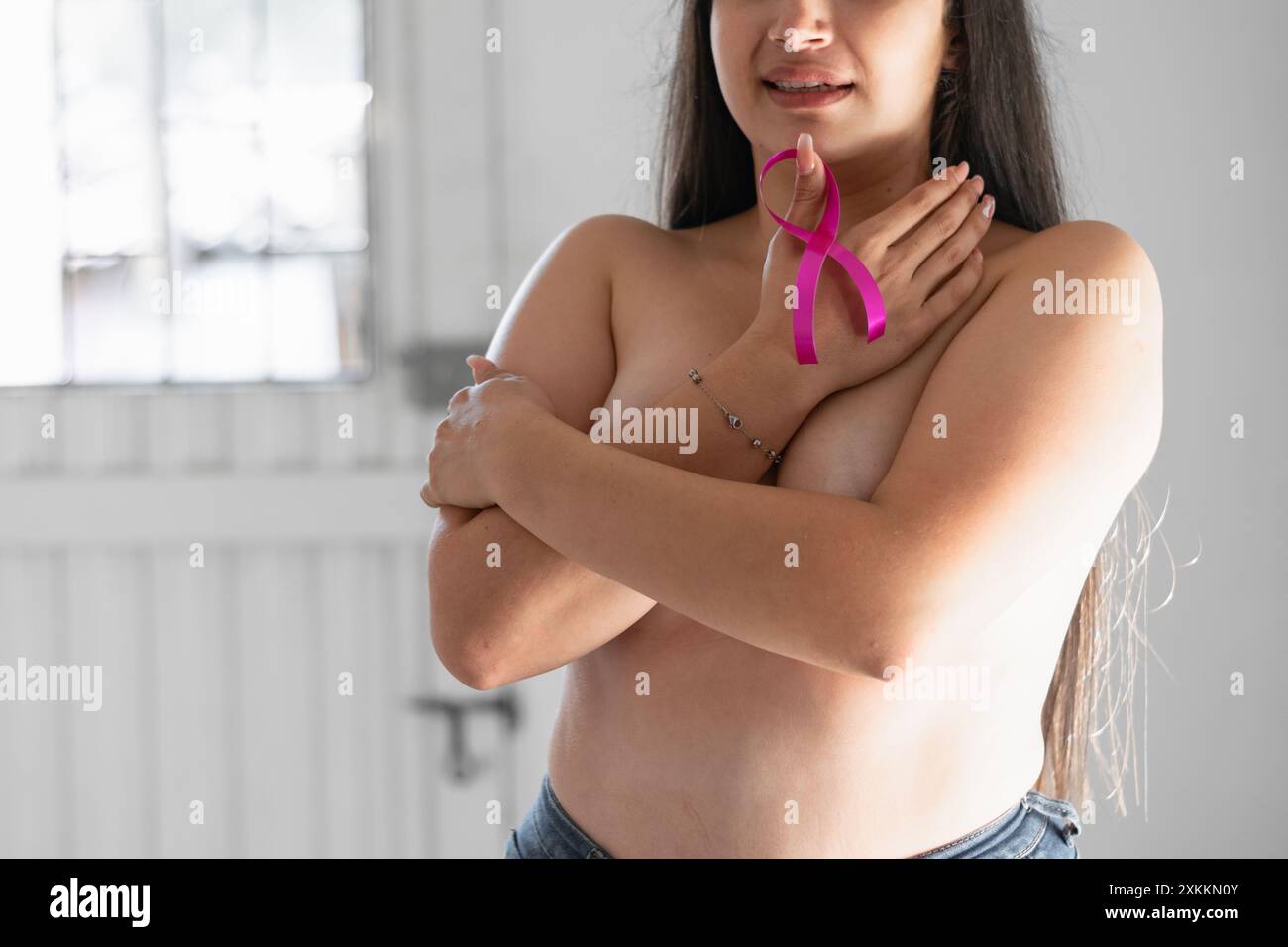 femme latina couvrant ses seins avec ses mains tout en tenant un ruban rose. lutte contre le cancer Banque D'Images