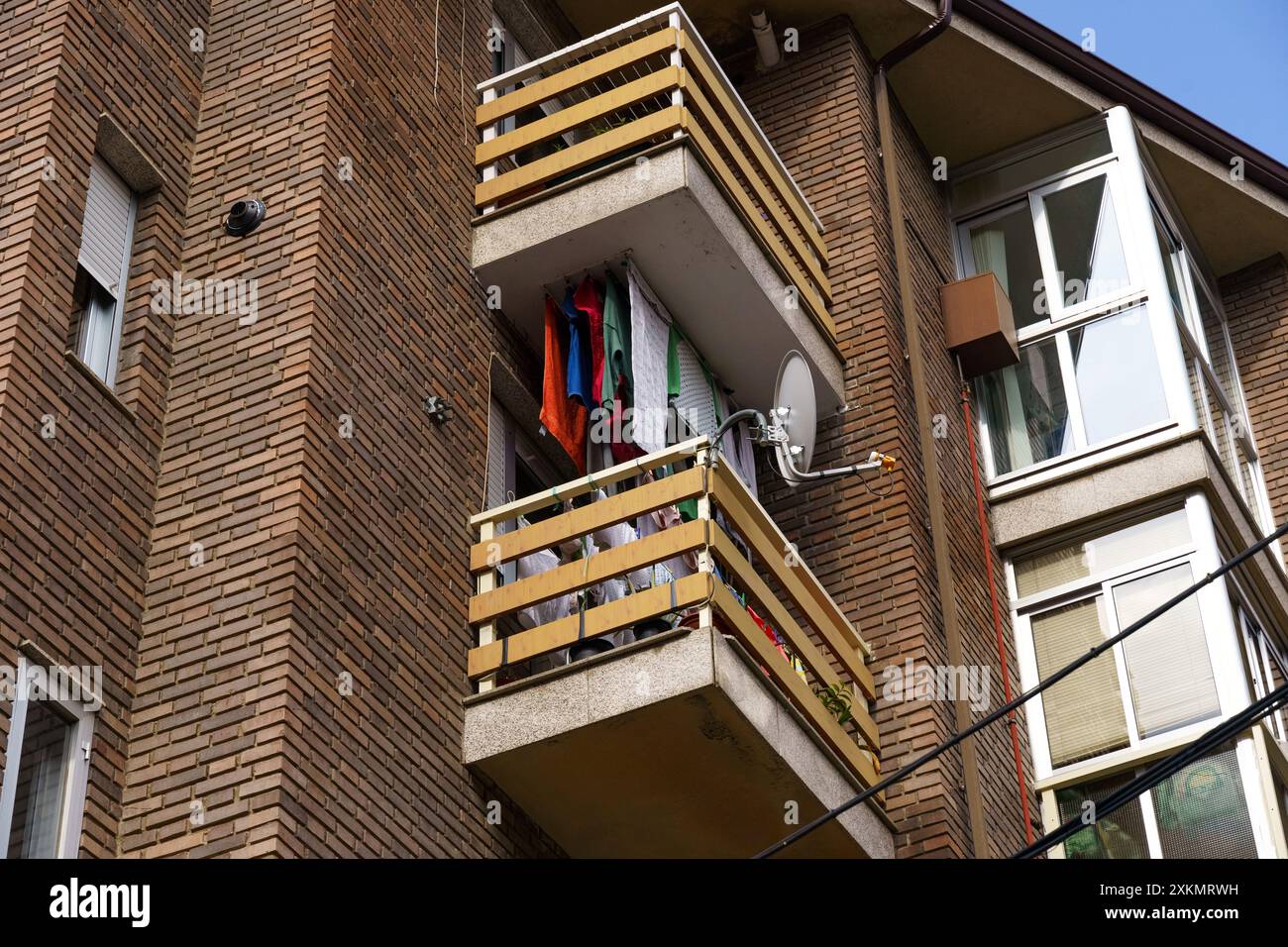 Une façade de bâtiment en briques avec un balcon sur lequel les vêtements aux couleurs vives sèchent au soleil. Banque D'Images