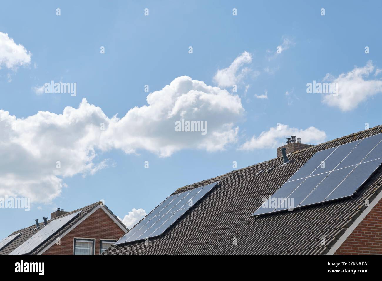 Cellules solaires bleues ou panneaux solaires sur les toits des maisons dans une rangée reflétant le ciel nuageux bleu. Concept d'énergie verte durable Banque D'Images