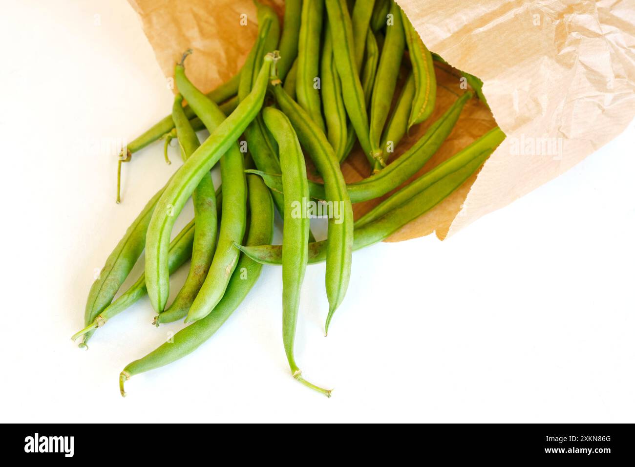 Gros plan de gousses de haricots verts mûrs biologiques dans un sac écologique en papier brun sur fond blanc. Concept d'environnement zéro déchet. Banque D'Images