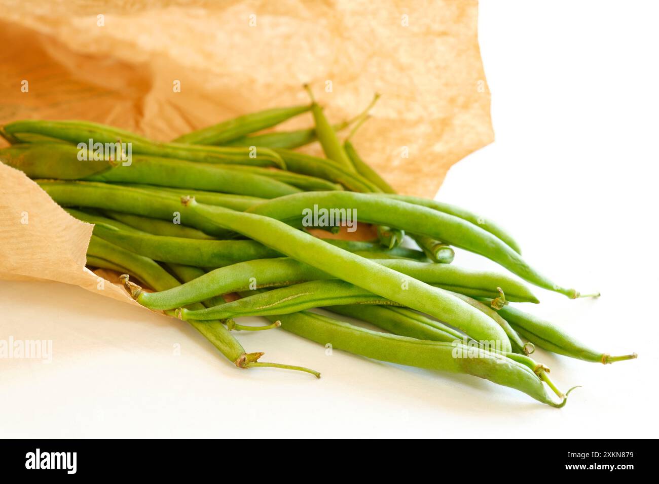 Gros plan de gousses de haricots verts mûrs biologiques dans un sac écologique en papier brun sur fond blanc. Concept d'environnement zéro déchet. Banque D'Images