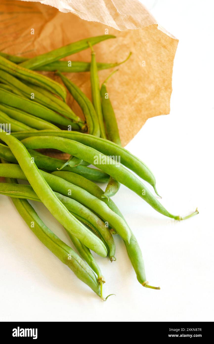 Gros plan de gousses de haricots verts mûrs biologiques dans un sac écologique en papier brun sur fond blanc. Concept d'environnement zéro déchet. Banque D'Images