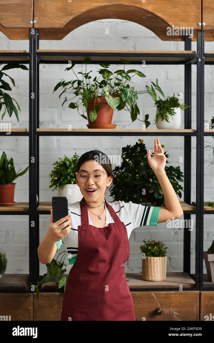 Une femme asiatique, propriétaire d'une usine, accueille avec enthousiasme ses clients avec un sourire et une vague. Banque D'Images