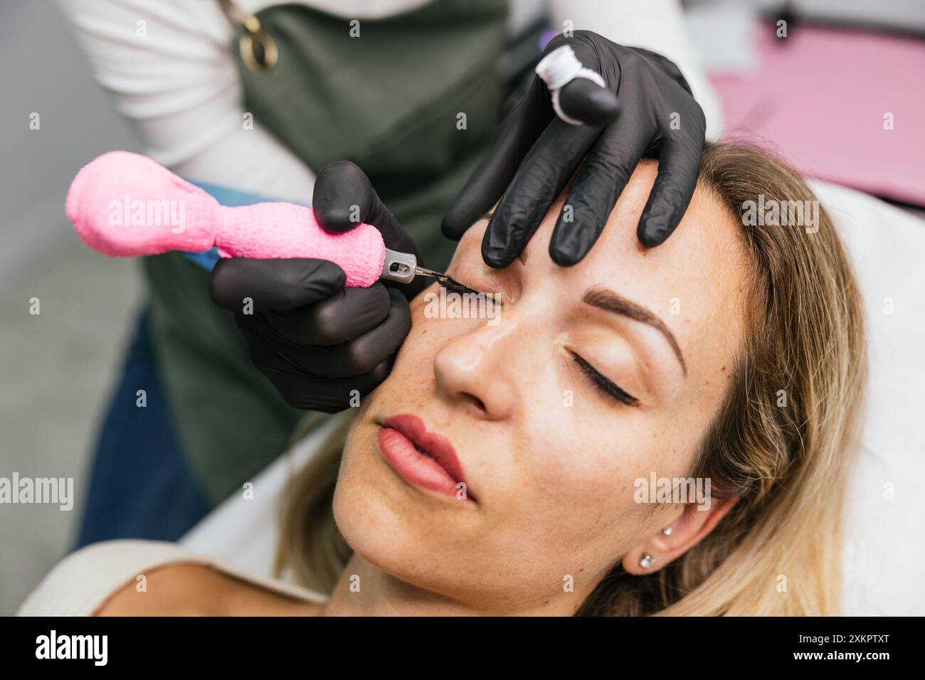 Gros plan d'une esthéticienne réalisant une micropigmentation de l'eye-liner de précision sur une cliente détendue dans une clinique de beauté moderne Banque D'Images