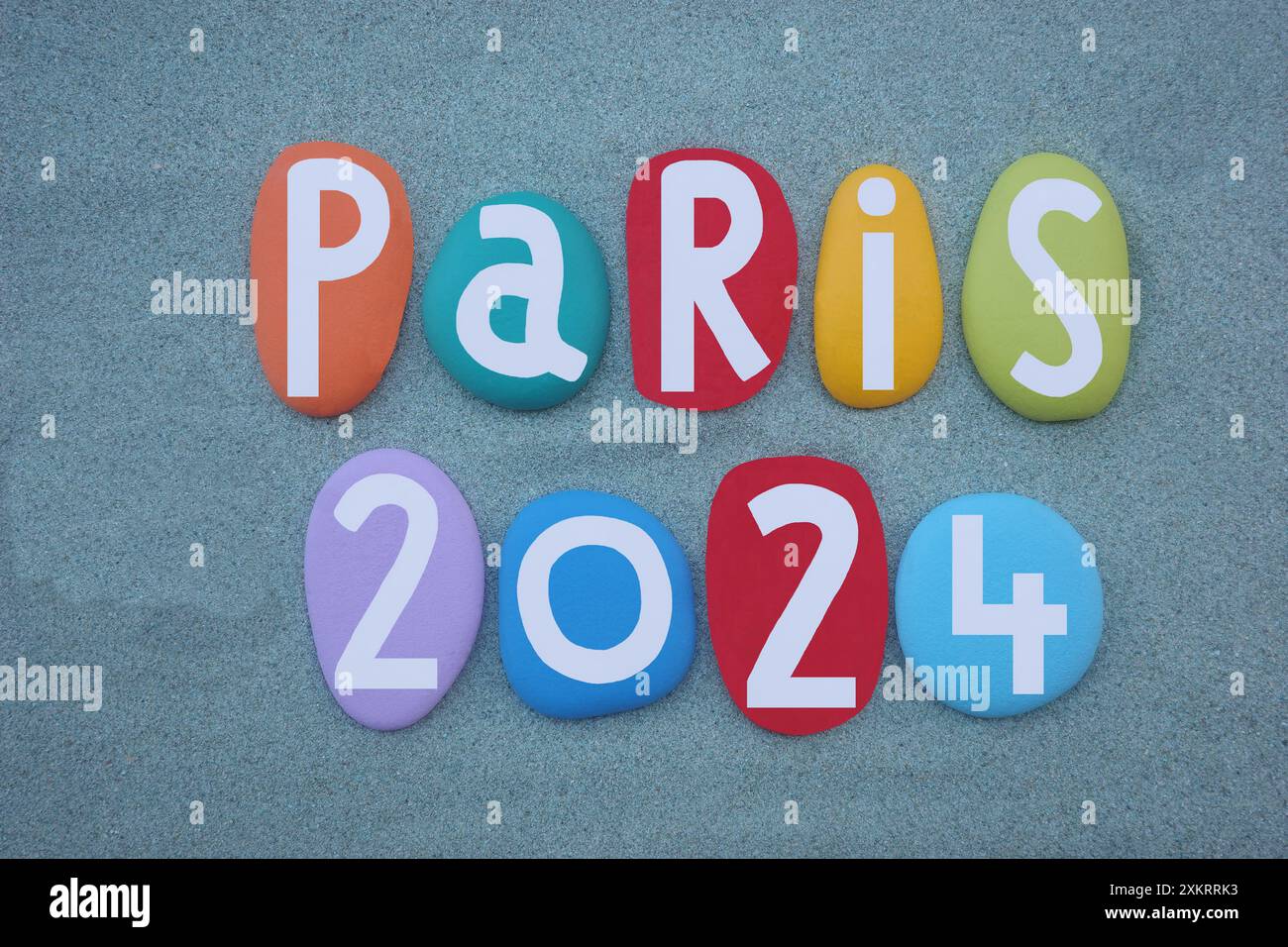 Paris 2024, logo créatif composé de lettres en pierre multicolores peintes à la main sur sable vert Banque D'Images