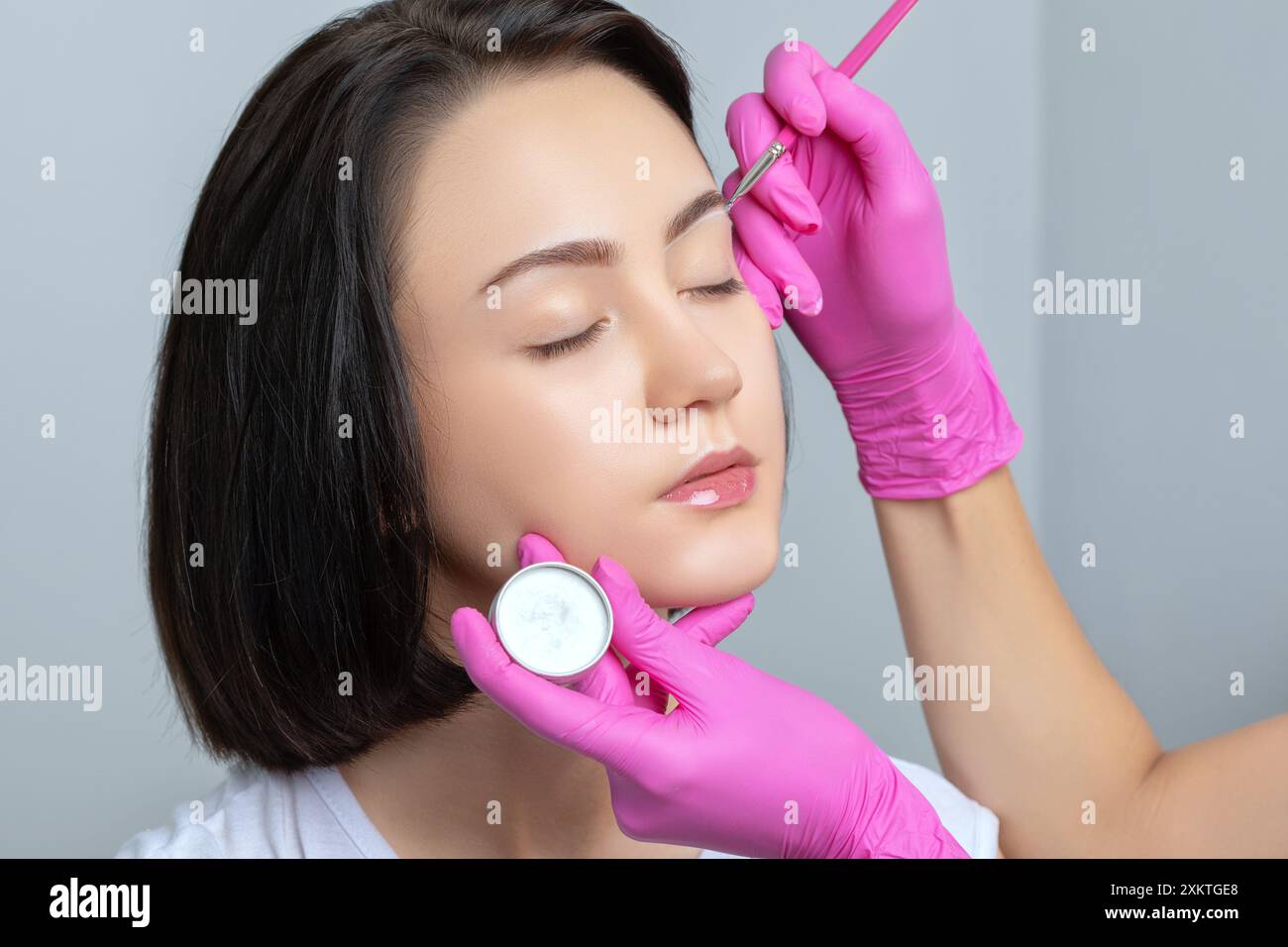Fille adolescente Brunette ayant un tatouage de maquillage permanent sur ses sourcils. Le maquilleur fait des marques avec de la pâte blanche pour le tatouage des sourcils. Professio Banque D'Images