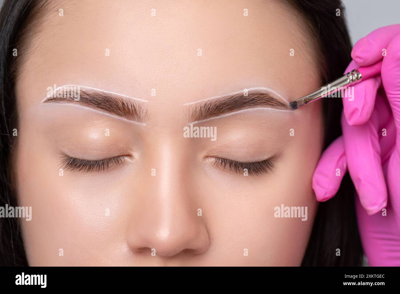 Fille adolescente Brunette ayant un tatouage de maquillage permanent sur ses sourcils. Le maquilleur fait des marques avec de la pâte blanche pour le tatouage des sourcils. Professio Banque D'Images