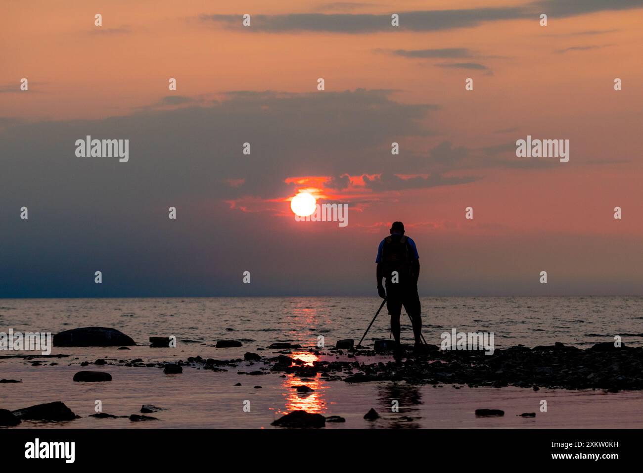Un photographe sur une plage rocheuse dresse une photo alors que le soleil se couche sur le lac Huron. Banque D'Images