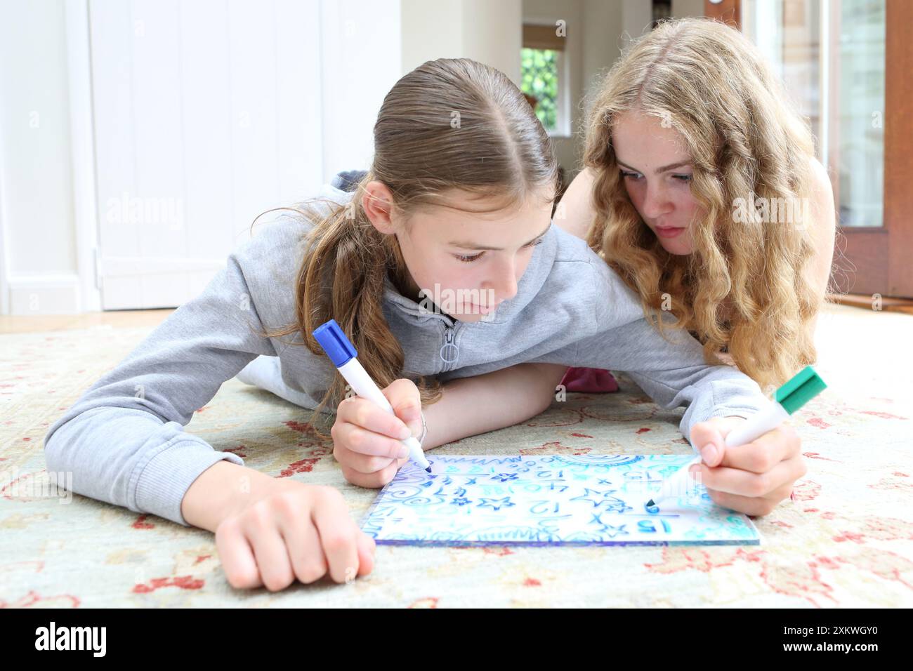 Filles faisant maths mathématiques allongées sur le sol écrivant sur le tableau blanc avec des stylos fractions mathématiques soeurs mathématiques éducation filles en STIM Banque D'Images