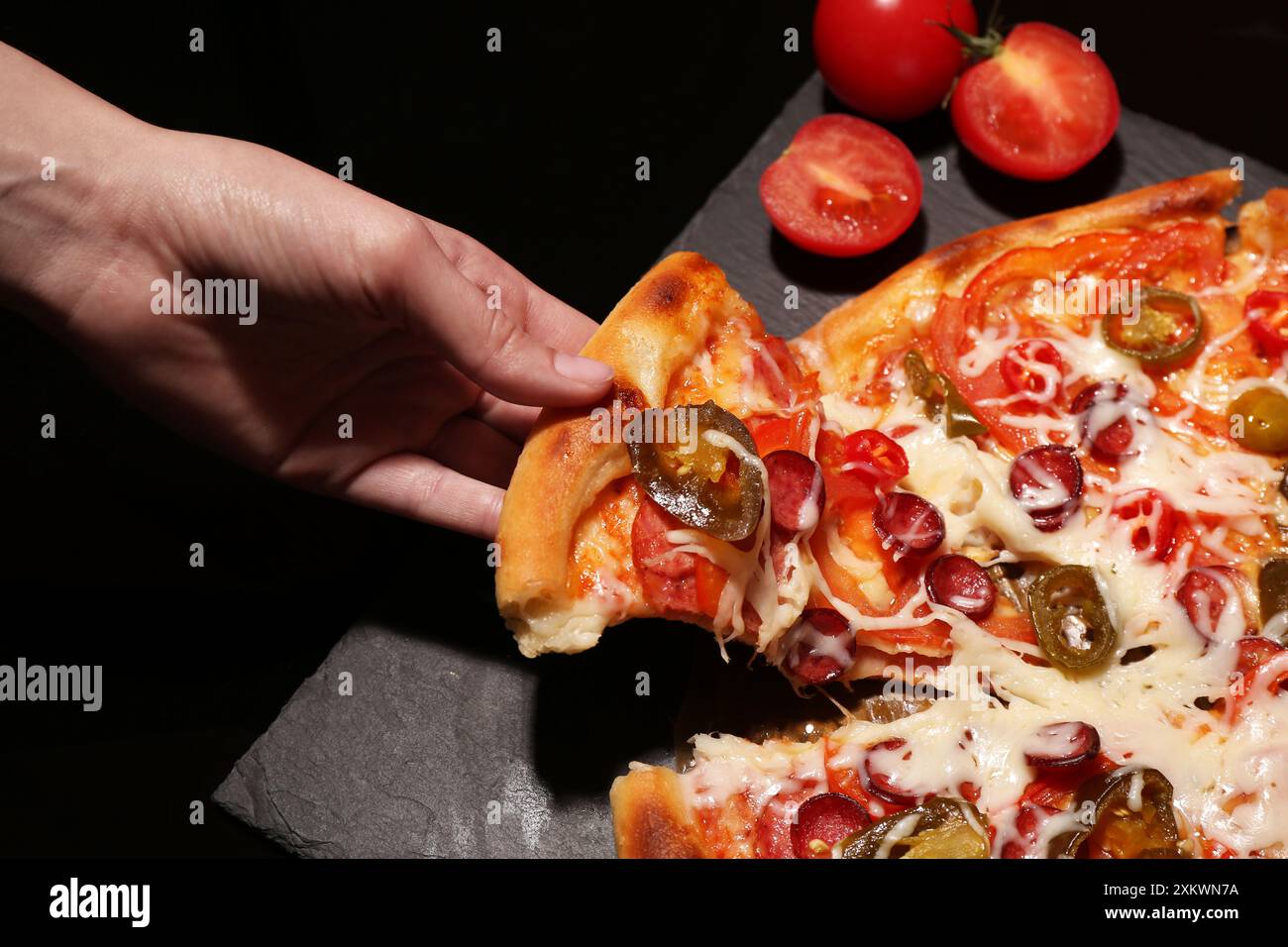 Femme prenant un morceau de délicieuse pizza Diablo sur fond noir, gros plan Banque D'Images