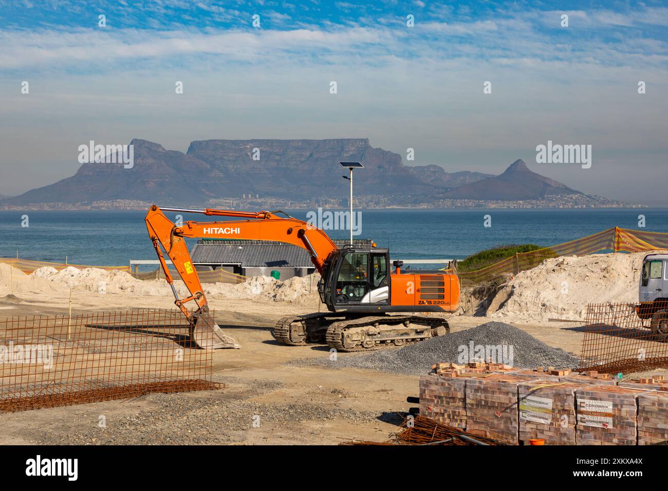 Chantier de construction à côté d'une plage au Cap avec une excavatrice Hitachi et divers autres matériaux de construction qui l'entourent. Banque D'Images
